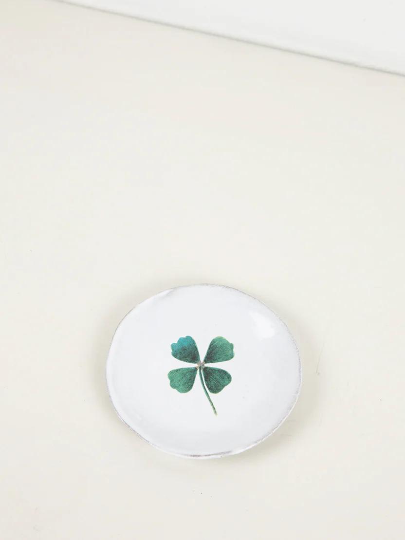 Small white ceramic dish with green four-leaf clover design. Minimalist style on light beige surface.