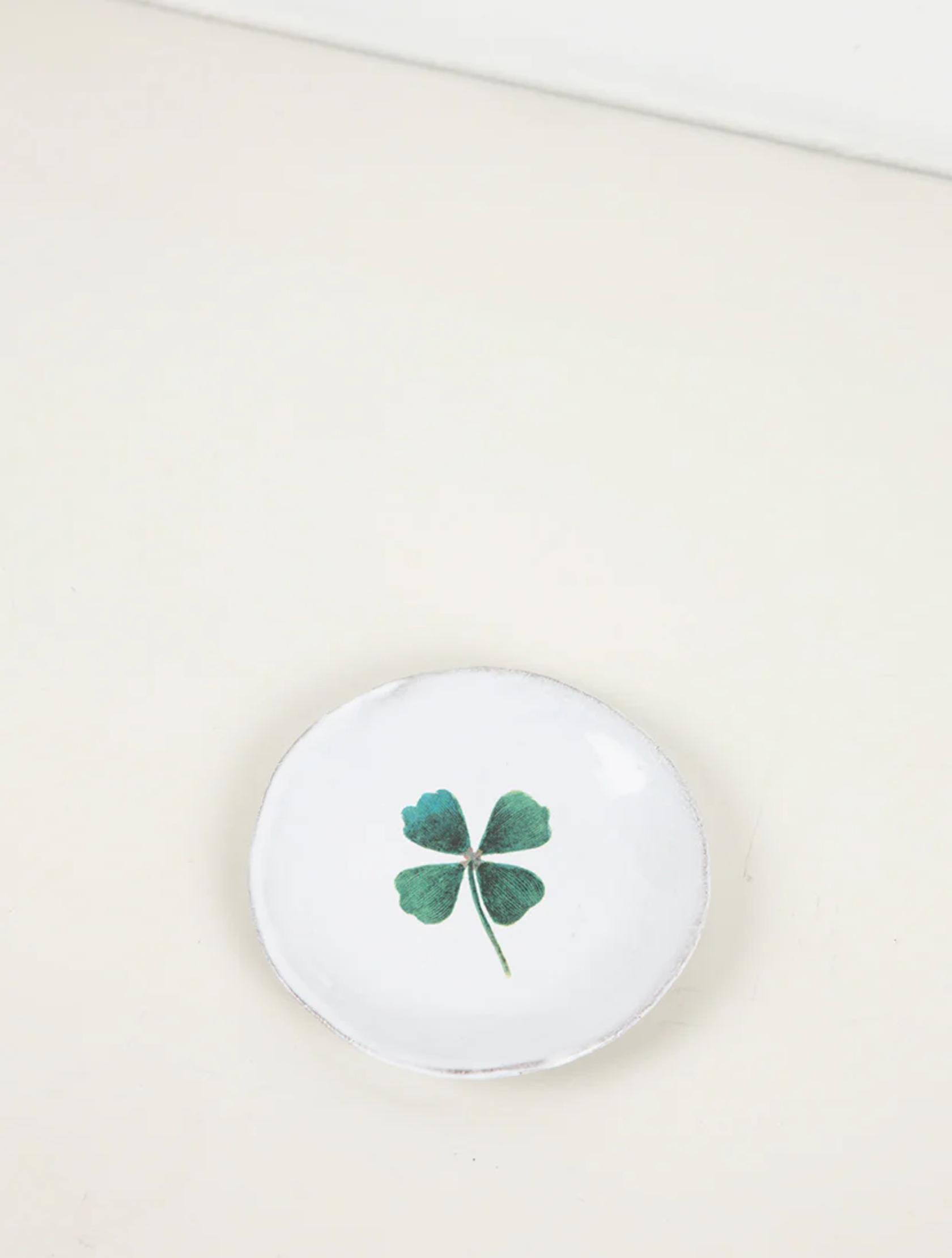Small white ceramic dish with green four-leaf clover design. Minimalist style on light beige surface.