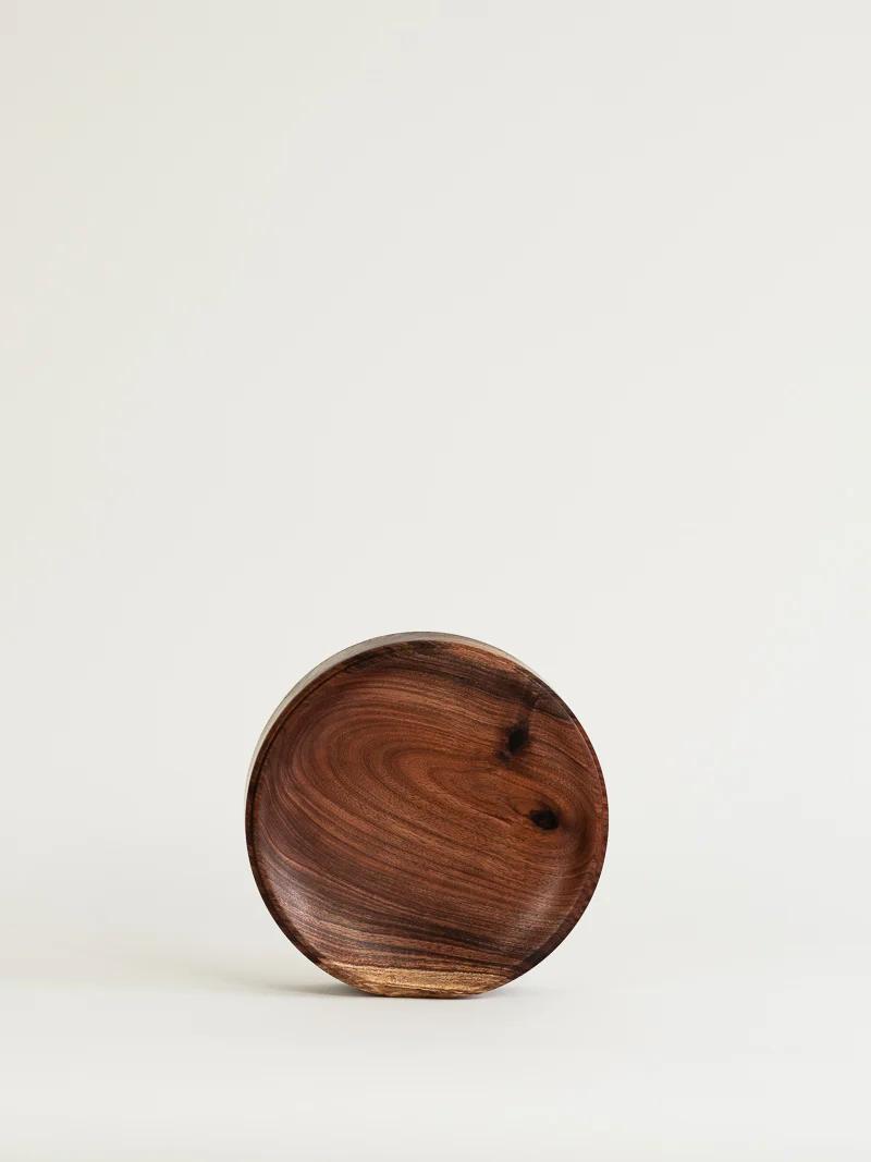 A round wooden bowl with a smooth, polished surface and natural wood grain pattern sits against a light background, reminiscent of discovering beautiful wooden objects during a park walk.