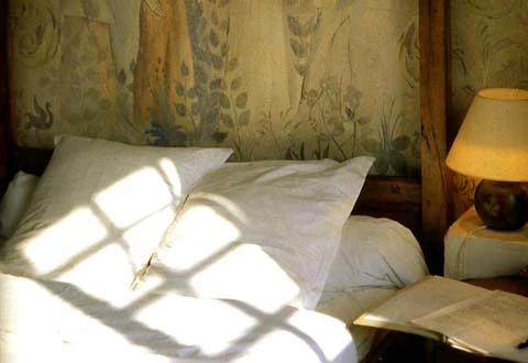 Sunlit bedroom with white bedding. Open book on bed. Decorative mural headboard. Window shadow across scene.