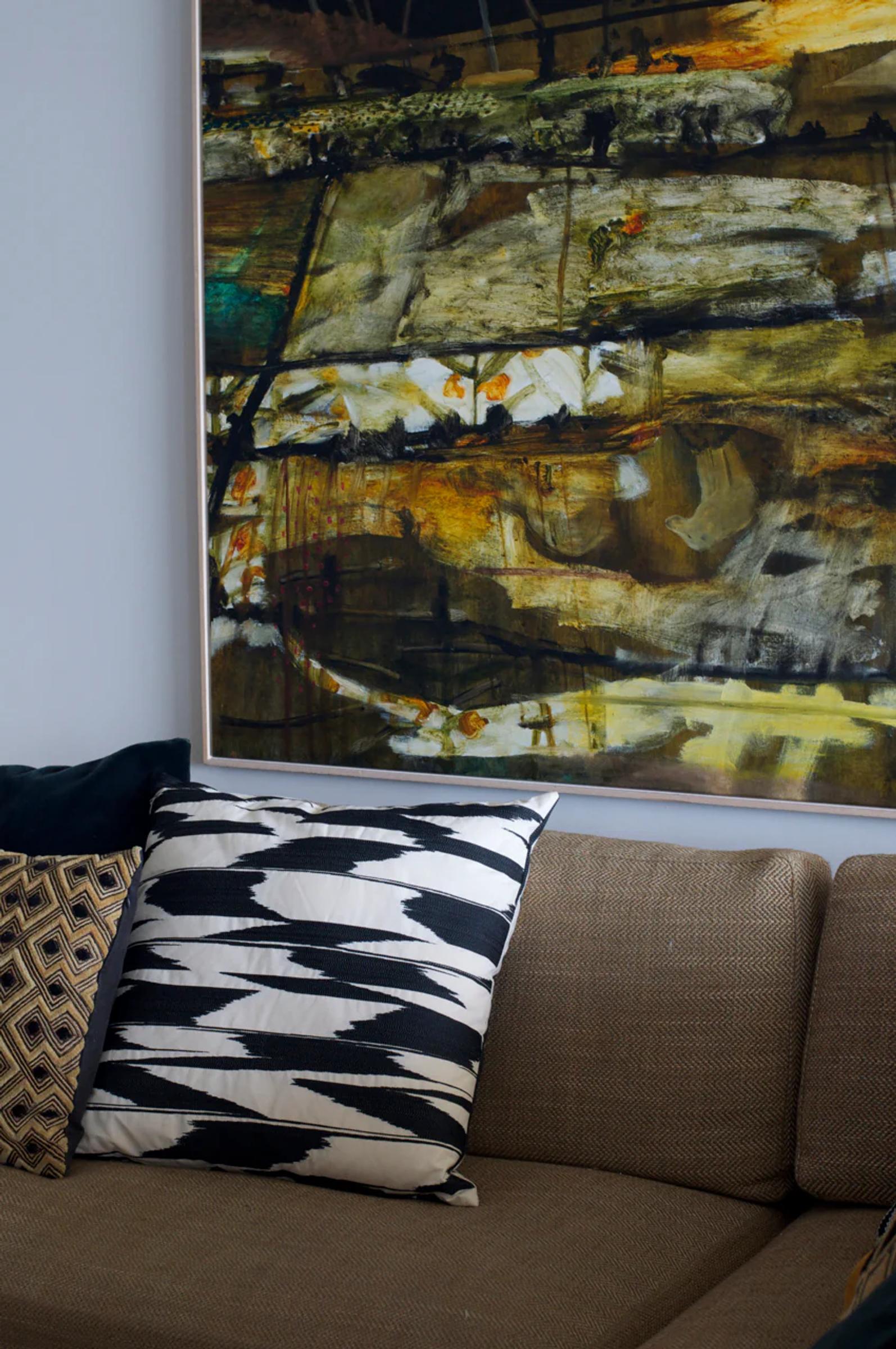 Brown sofa with patterned pillows below large abstract painting. Artwork features earthy tones of browns, greens, and yellows in living room setting.