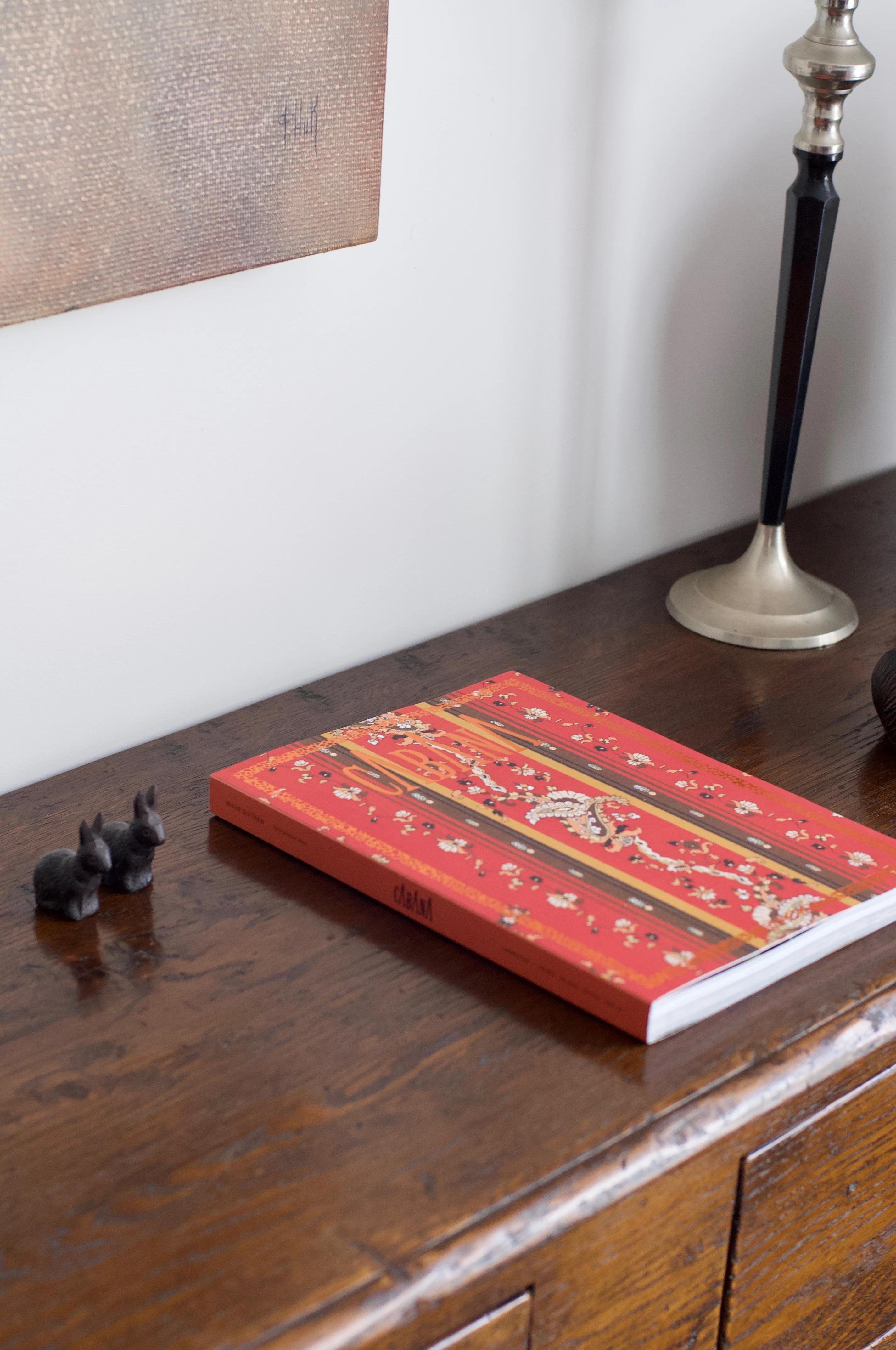 Red CABANA Magazine on table with black animal figurines. Partial view of lamp and textured artwork.