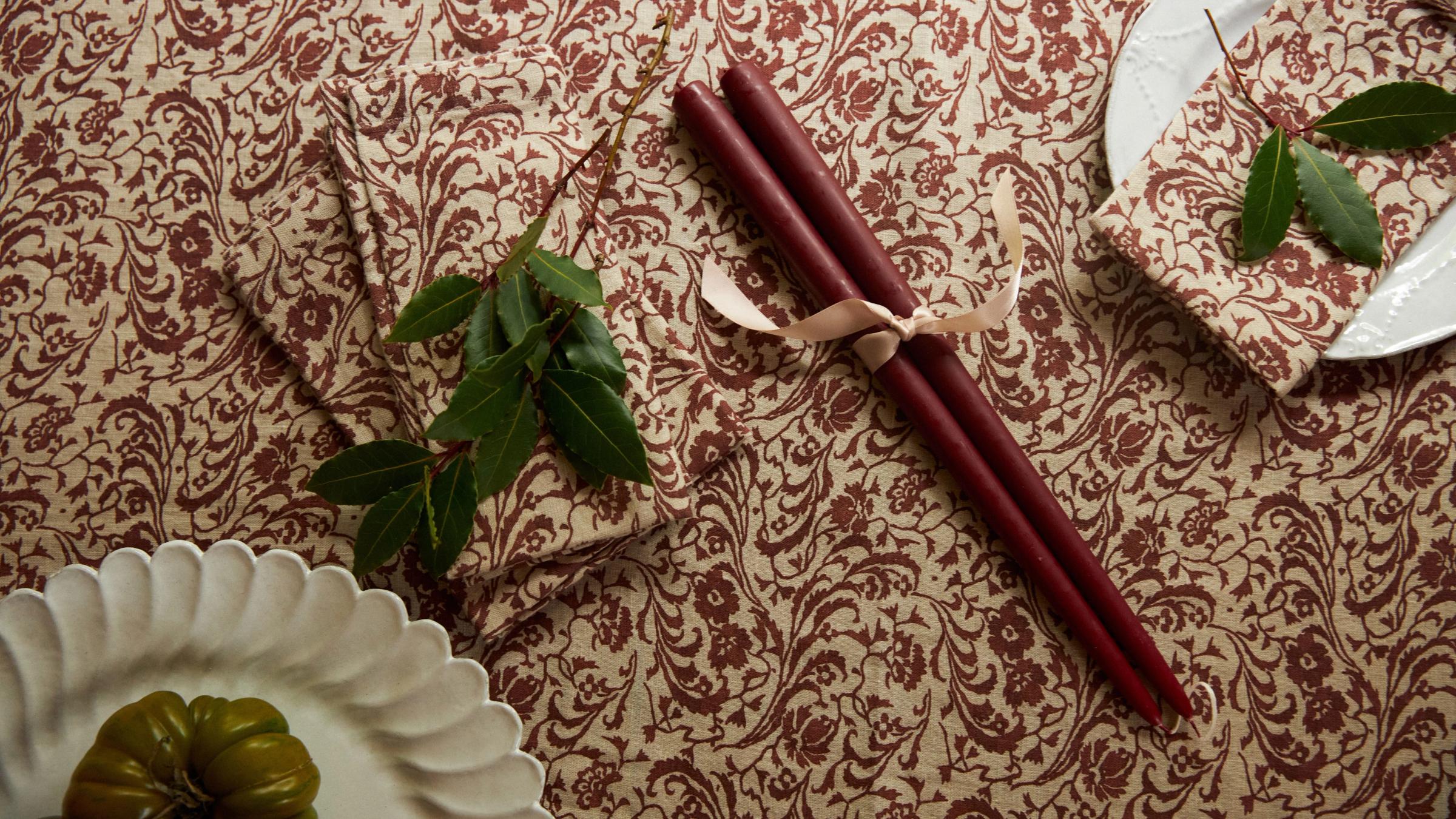 Red patterned tablecloth with green bay leaves, white plates and red candles
