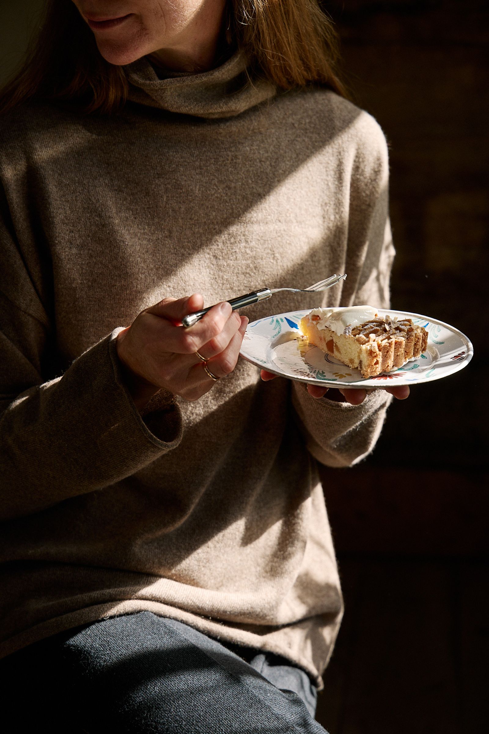 woman sitting in sun begins to eats slice of cake with fork
