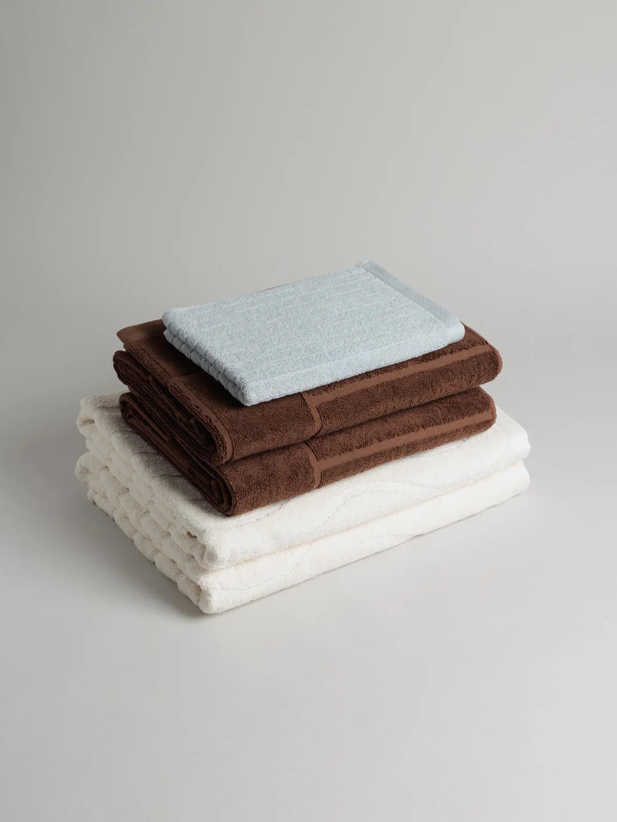 Stack of folded towels: two white at bottom, two brown in middle, light blue on top. Neutral background.