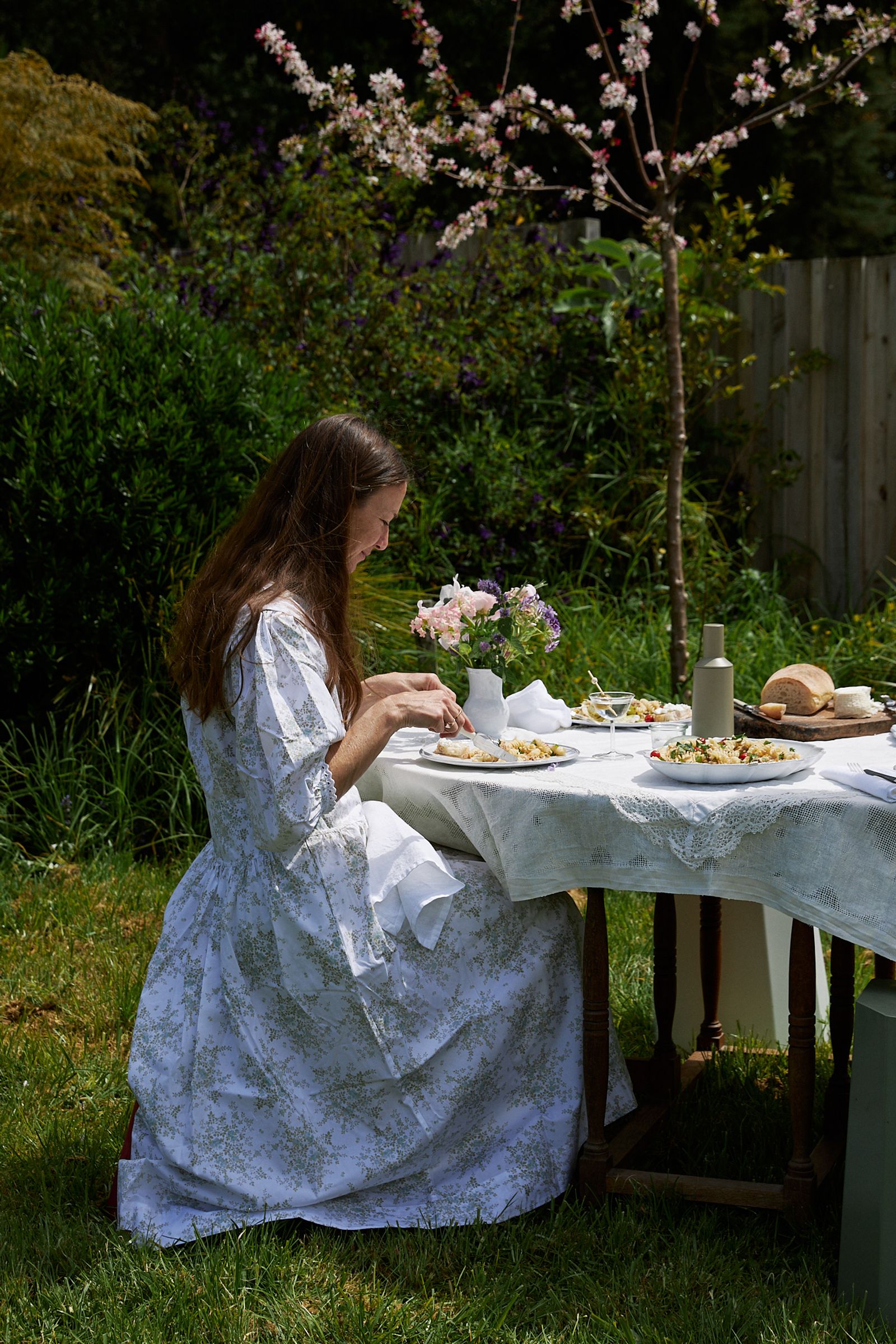 woman sits at a table in the garden eating lunch in the sun