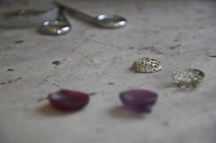 Jewellery workbench with red and purple stones, metal components. Blurred tools in background suggest nature-inspired designer's workspace.