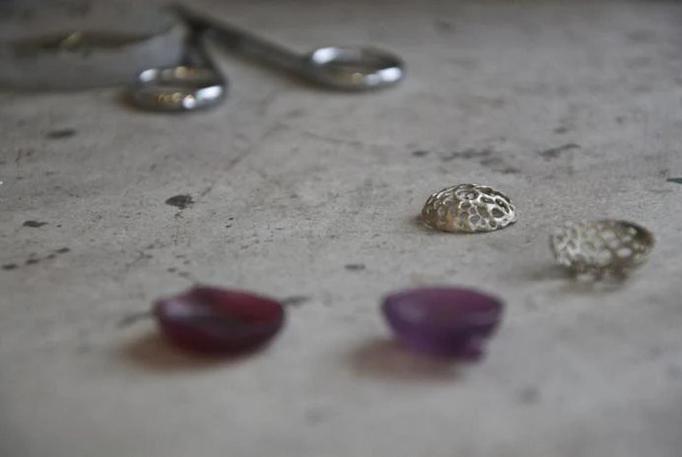 Jewellery workbench with red and purple stones, metal components. Blurred tools in background suggest nature-inspired designer's workspace.