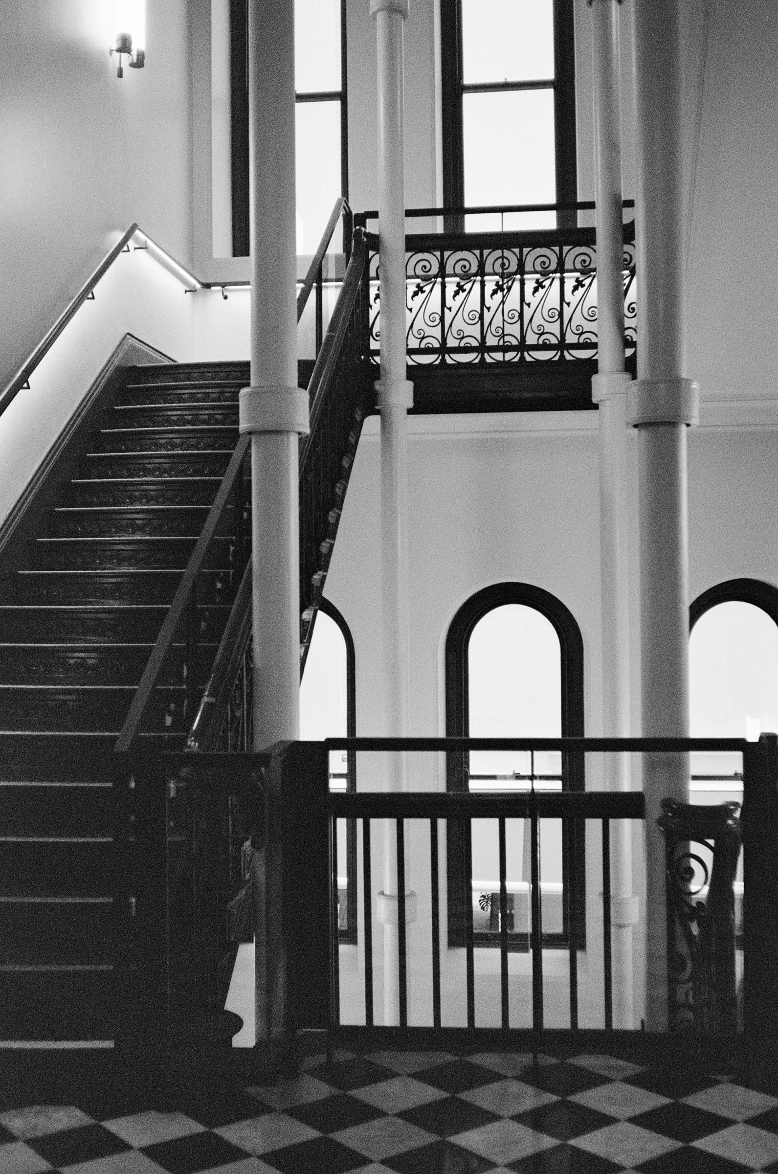 black and white image of a 1800s building with checkerboard flooring and grand staircase