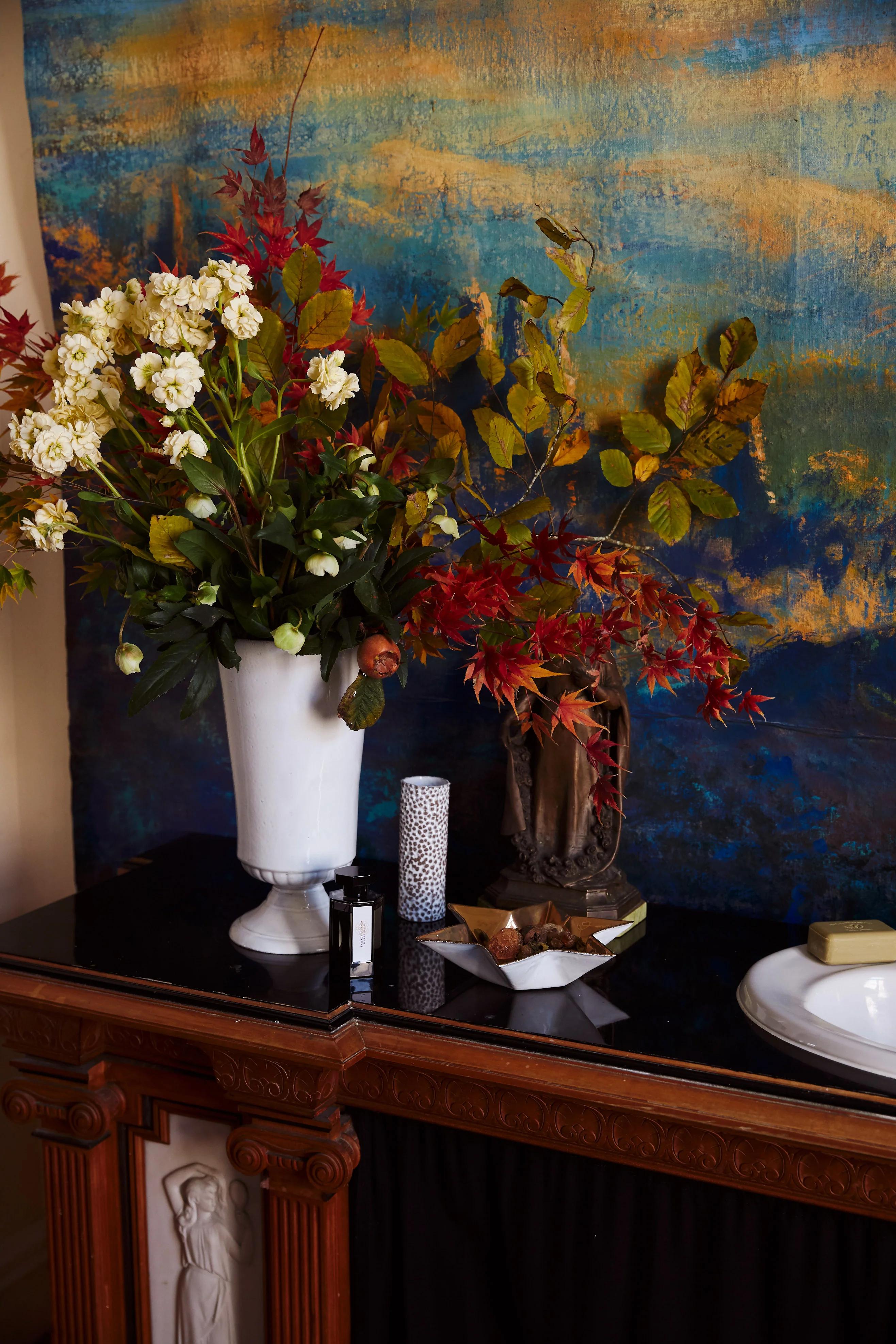 Dark table with flower vases, candle, and soap dish. Colourful painting in background. Setup perfect for long winter solstice baths.