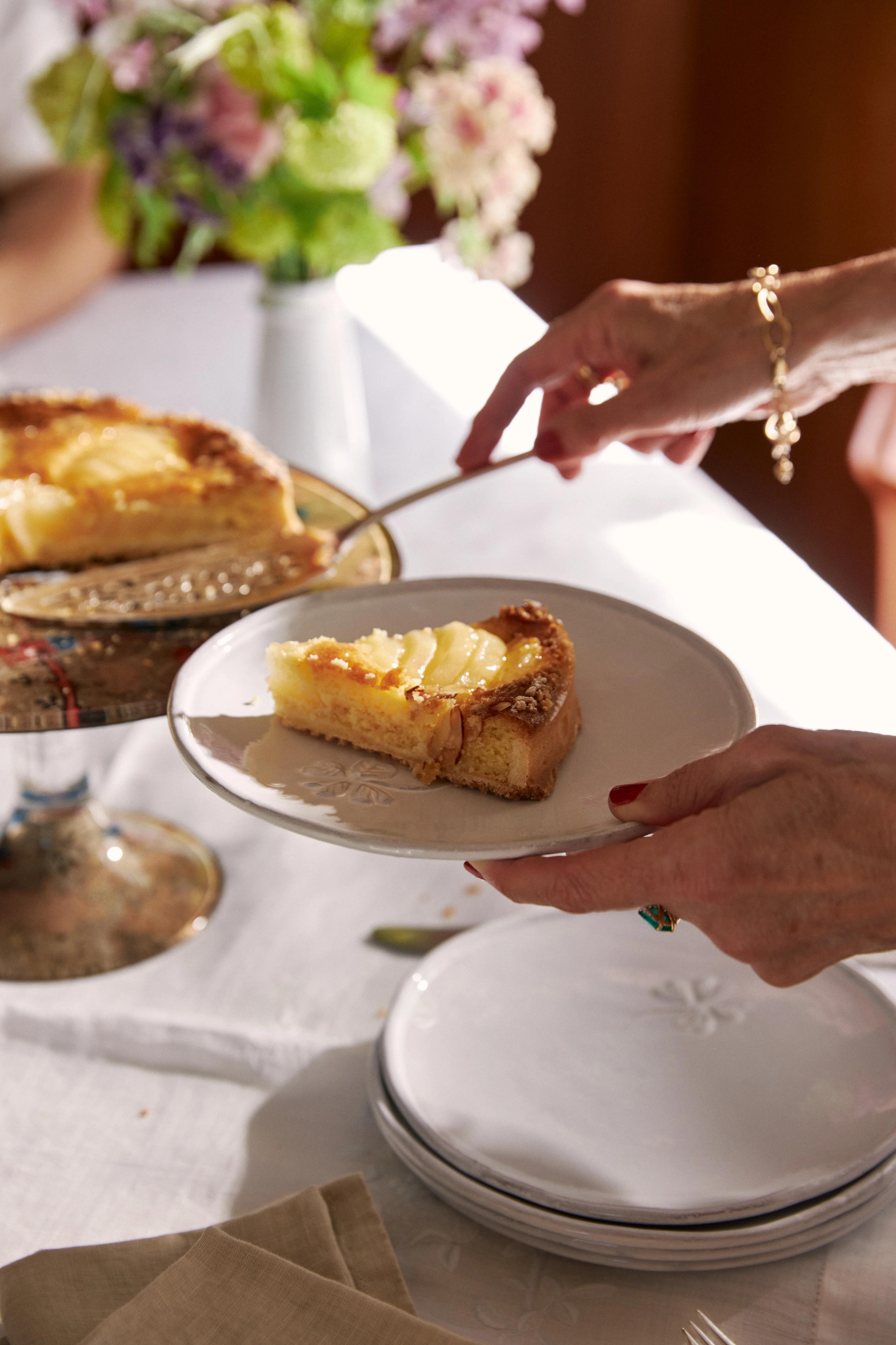 A woman serving a plate with a slice of pear tart while she places serving slice back onto cake stand