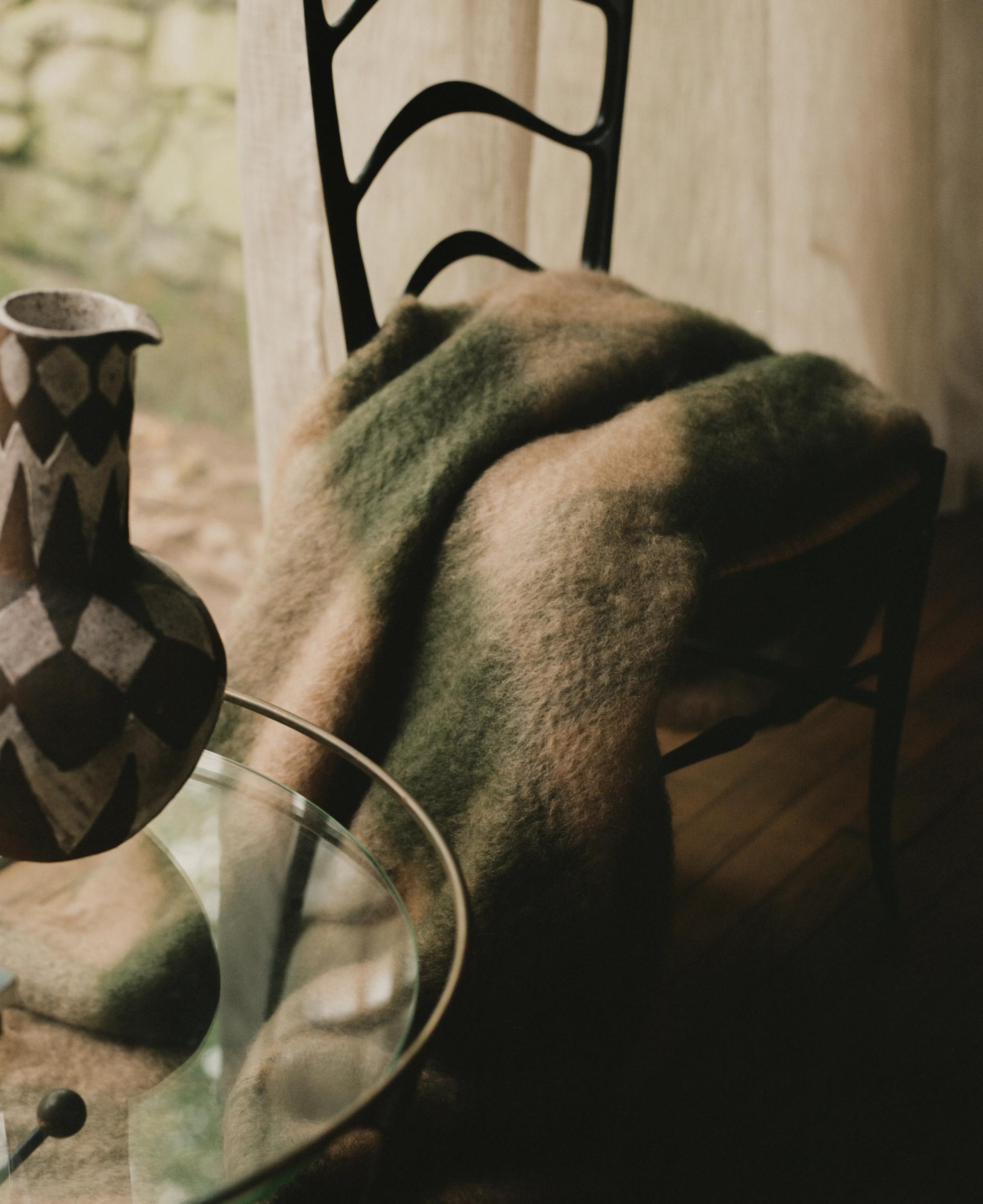 a cropped image of a chair, blanket next to a coffee table with painted jug
