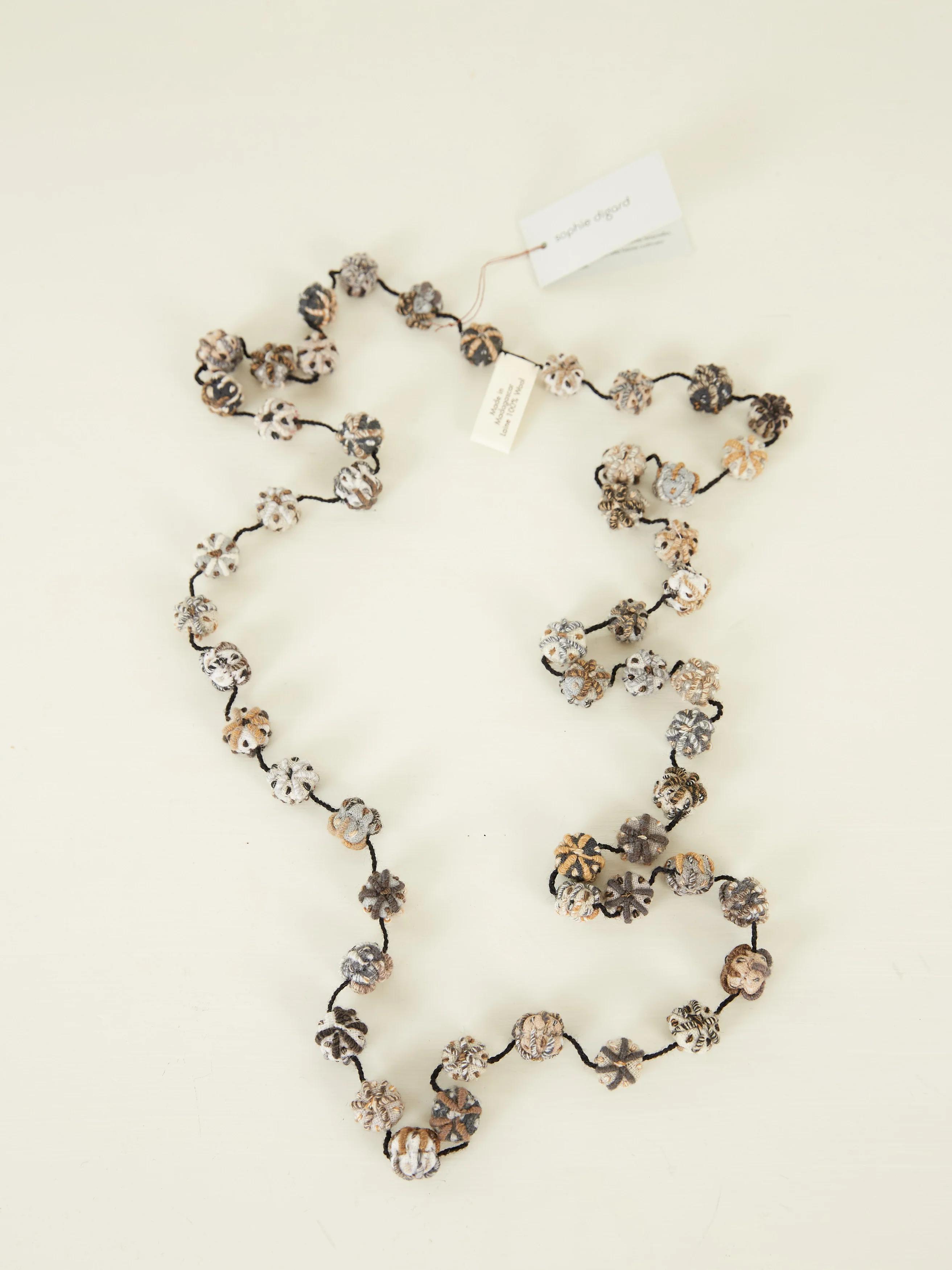 A long necklace by Sophie Digard with crocheted flower-shaped beads in white, black, and brown on a black thread.