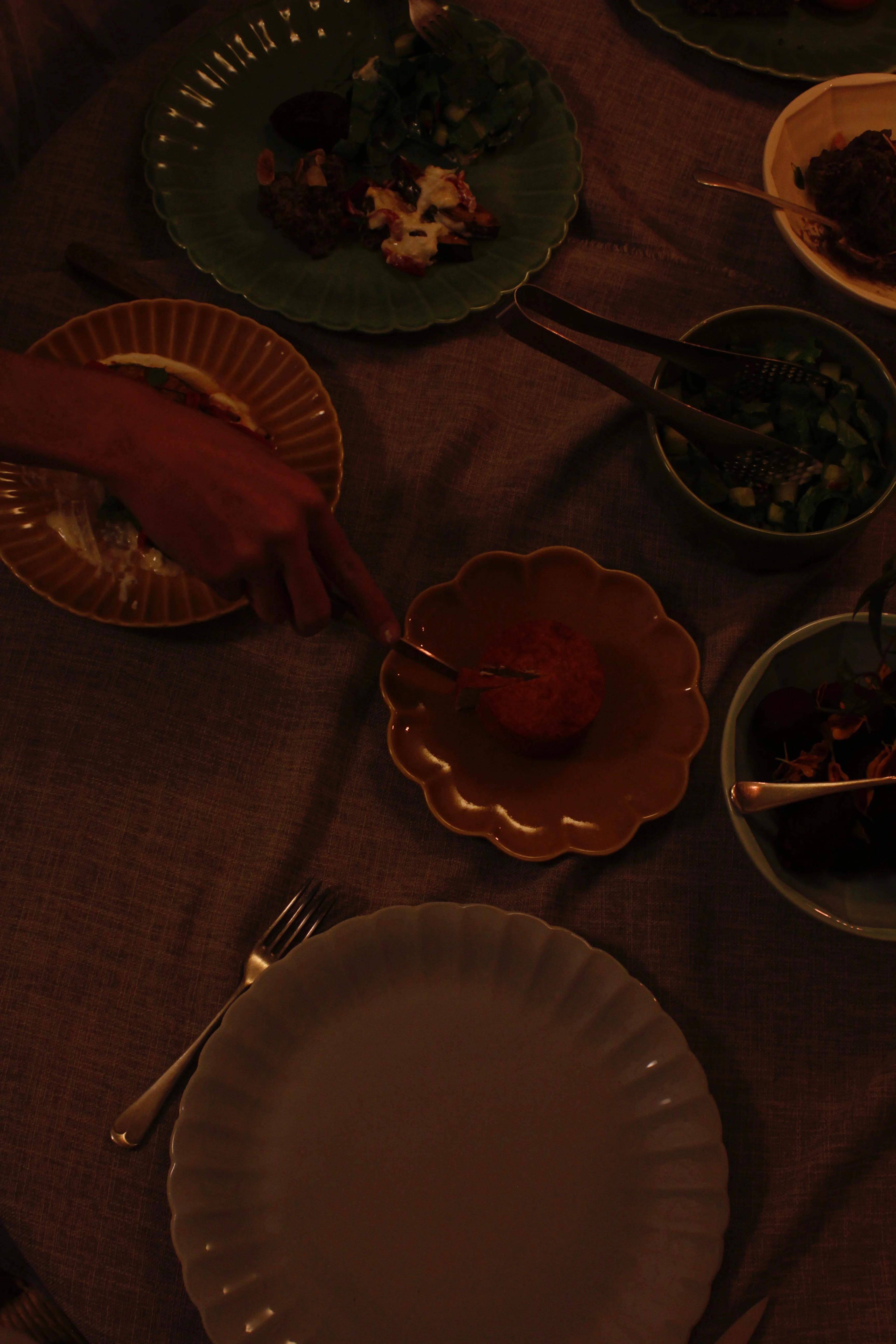 A hand points to an orange dish on a brown plate amidst a communal dining setting described in Falastin: A Cookbook.