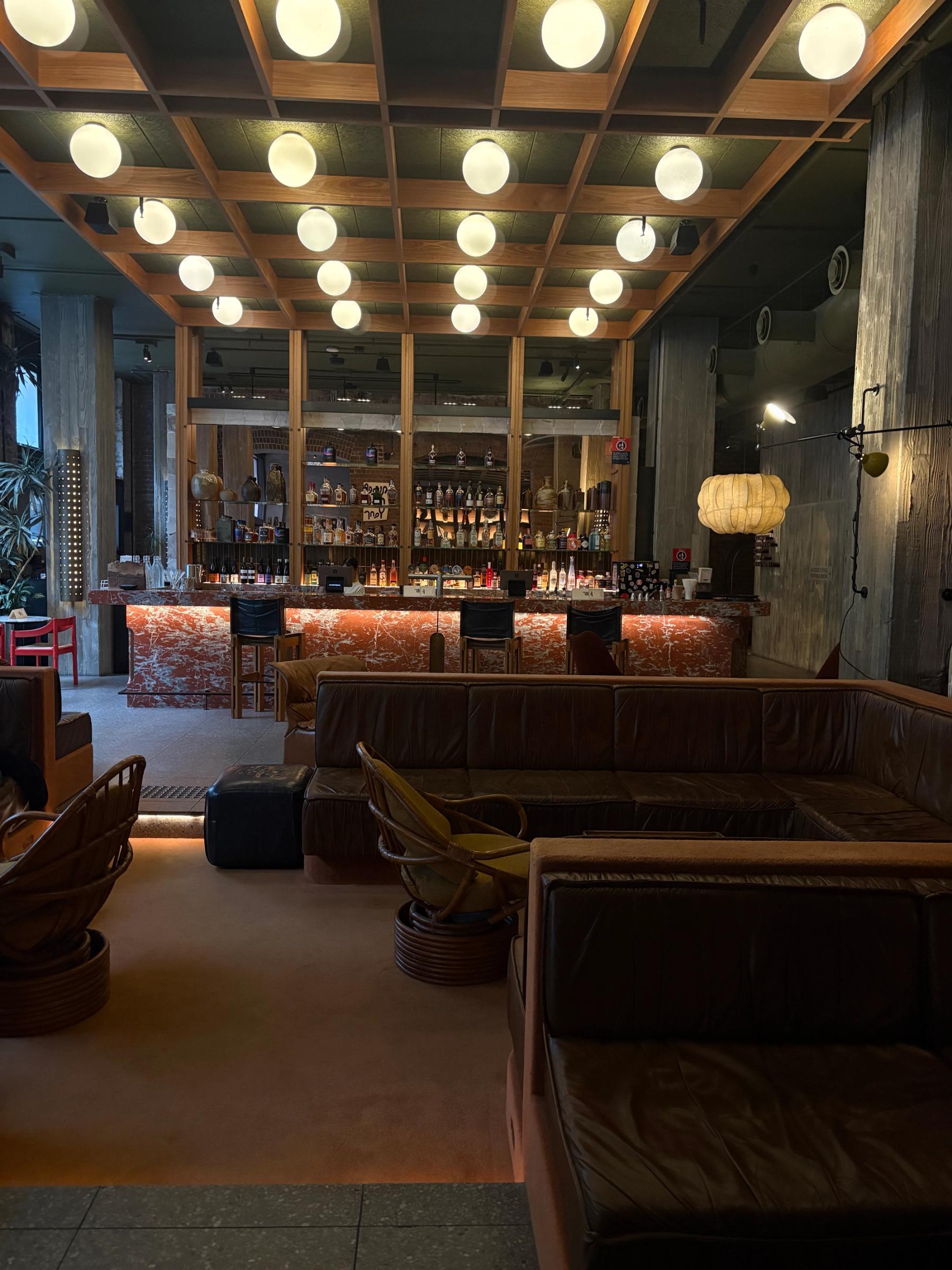 low lit lounge area of hotel with sunken leather couches and cane chairs with a marble bar in the background