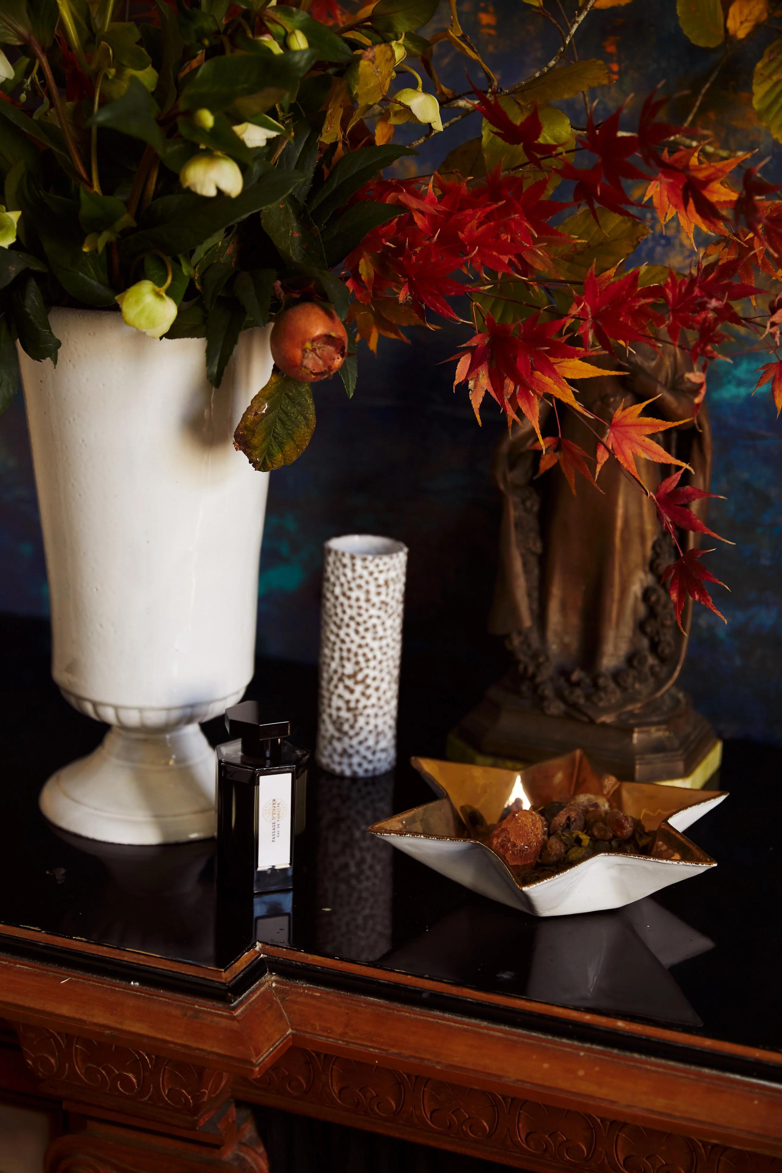 Decorative table with white vase, bronze sculpture, candle holder, perfume bottle, and dried botanicals. Perfect setting for savouring red wine.