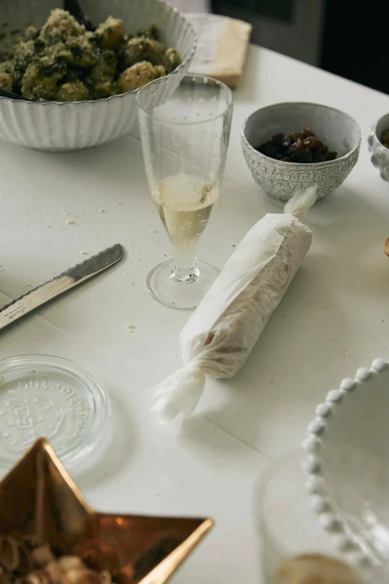 A white table set with a plate of food, a half-filled glass, bowls, and a decorative star-shaped dish—ideal for holiday feasting with Tessuti family recipes.