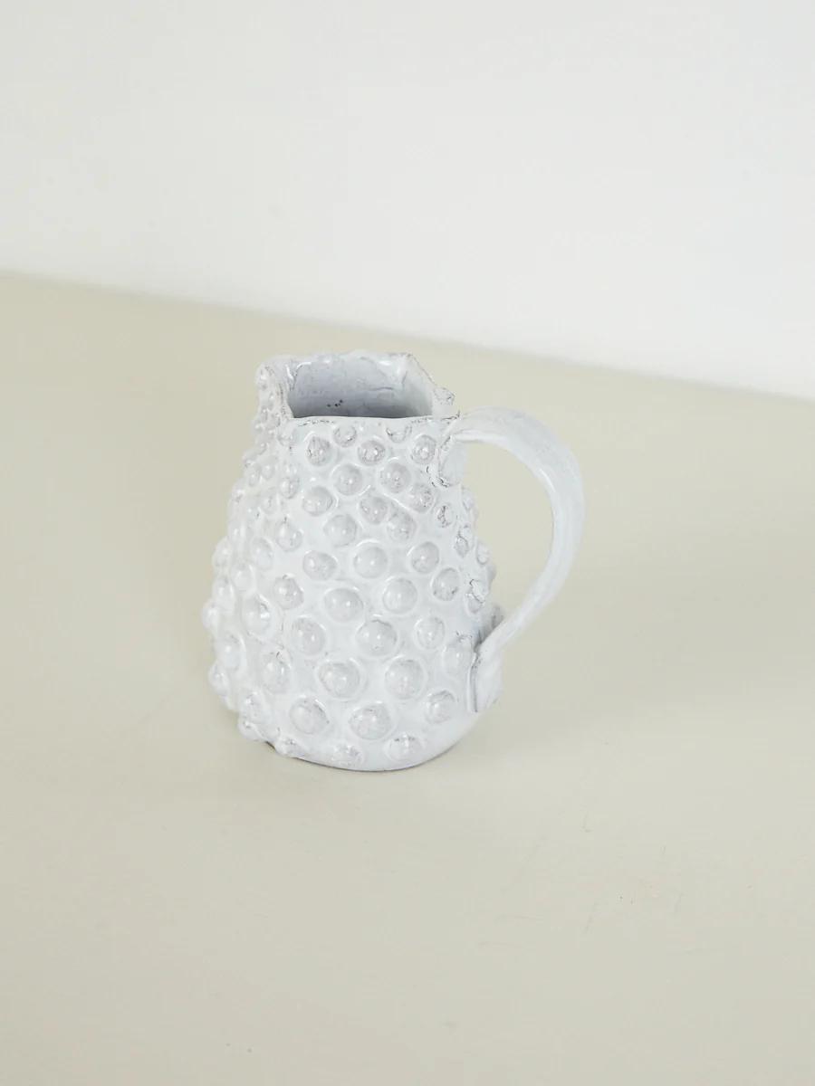 Small white ceramic pitcher with textured surface. Circular bumps, handle. Light-colored surface.