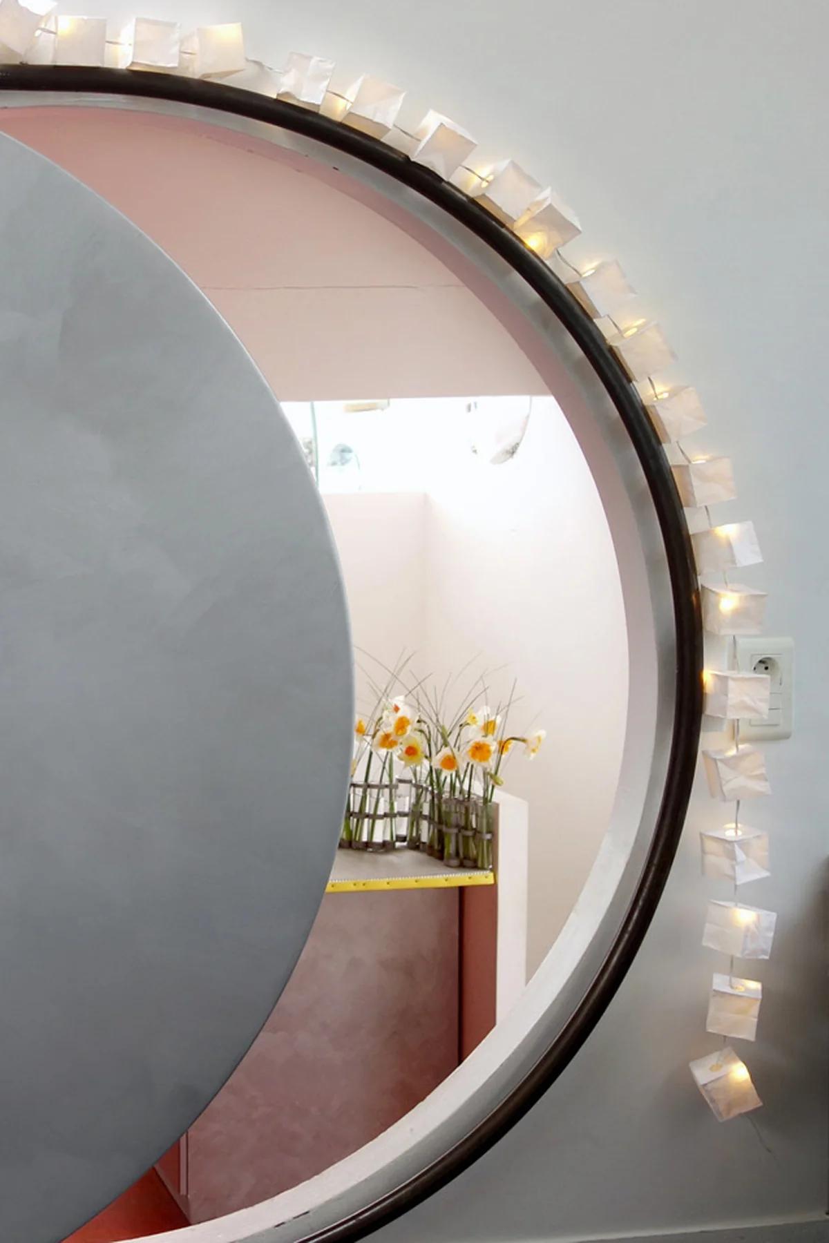 Circular doorway with glowing white paper lanterns. Yellow and white flowers in vases beyond, creating inviting atmosphere.