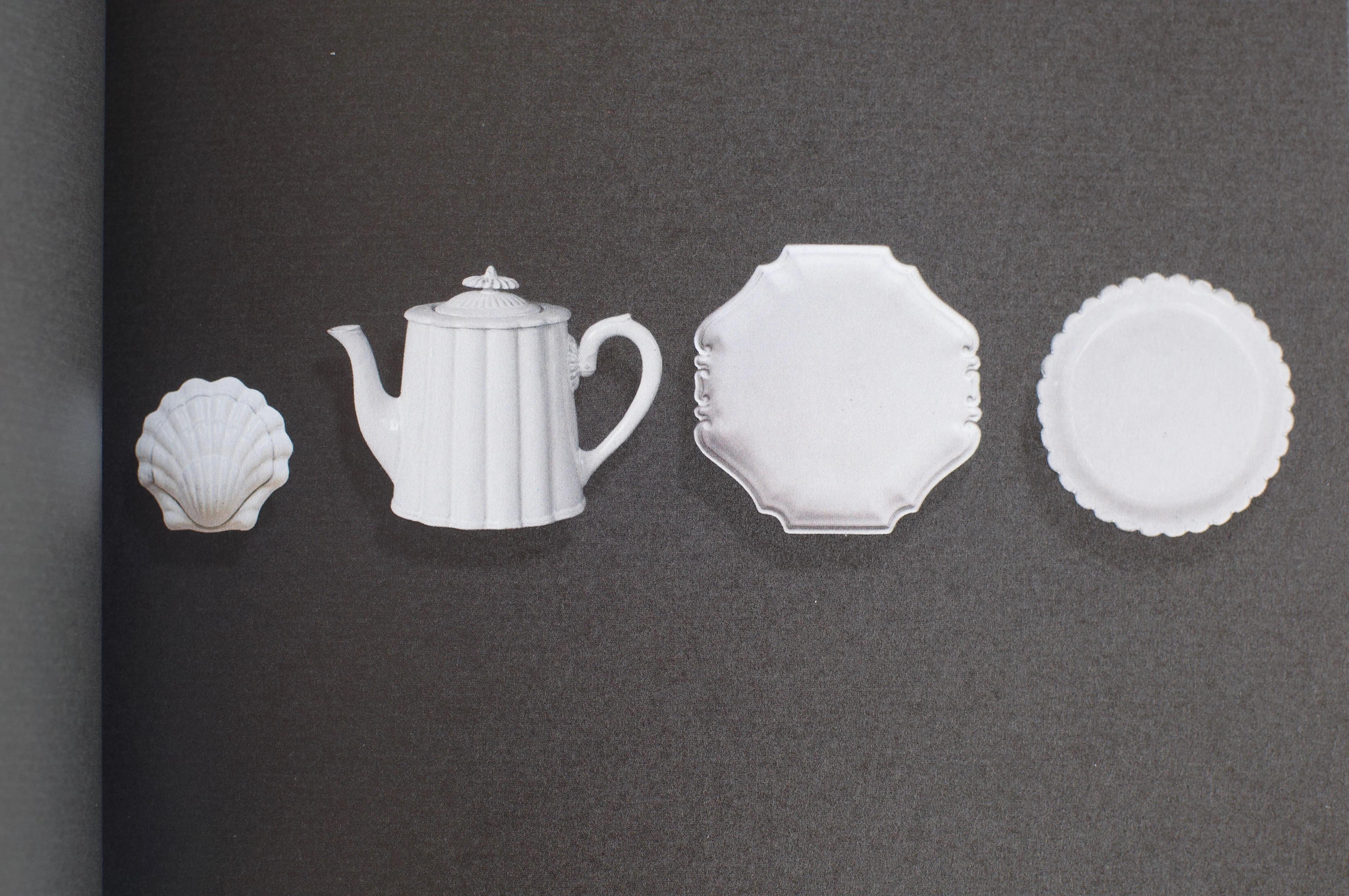 Four white porcelain items on a dark background: a shell-shaped dish, teapot, square plate with scalloped edges, and a textured round plate.