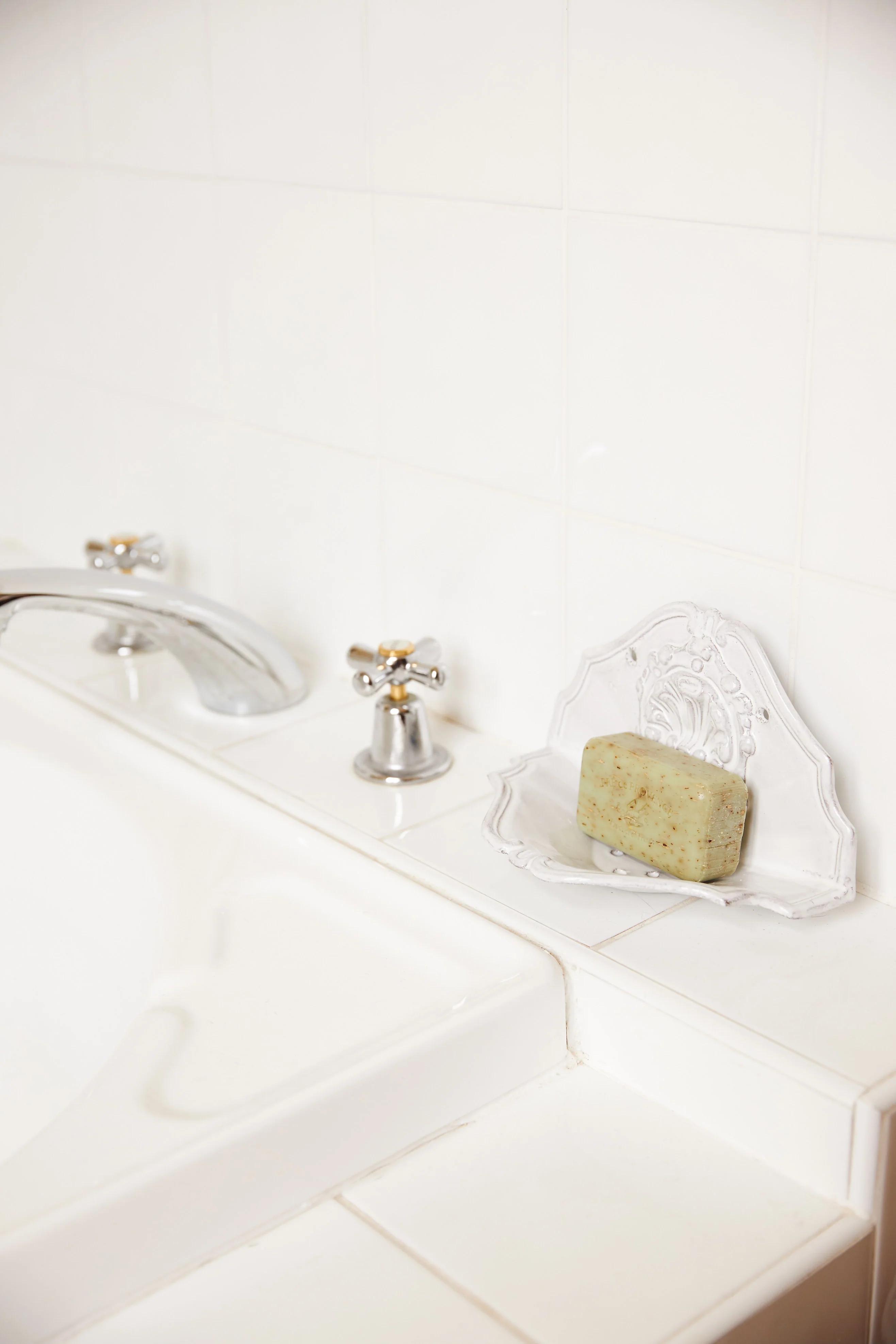 White bathtub with silver faucet against tiled wall. Ornate soap dish with speckled green soap on tub edge.