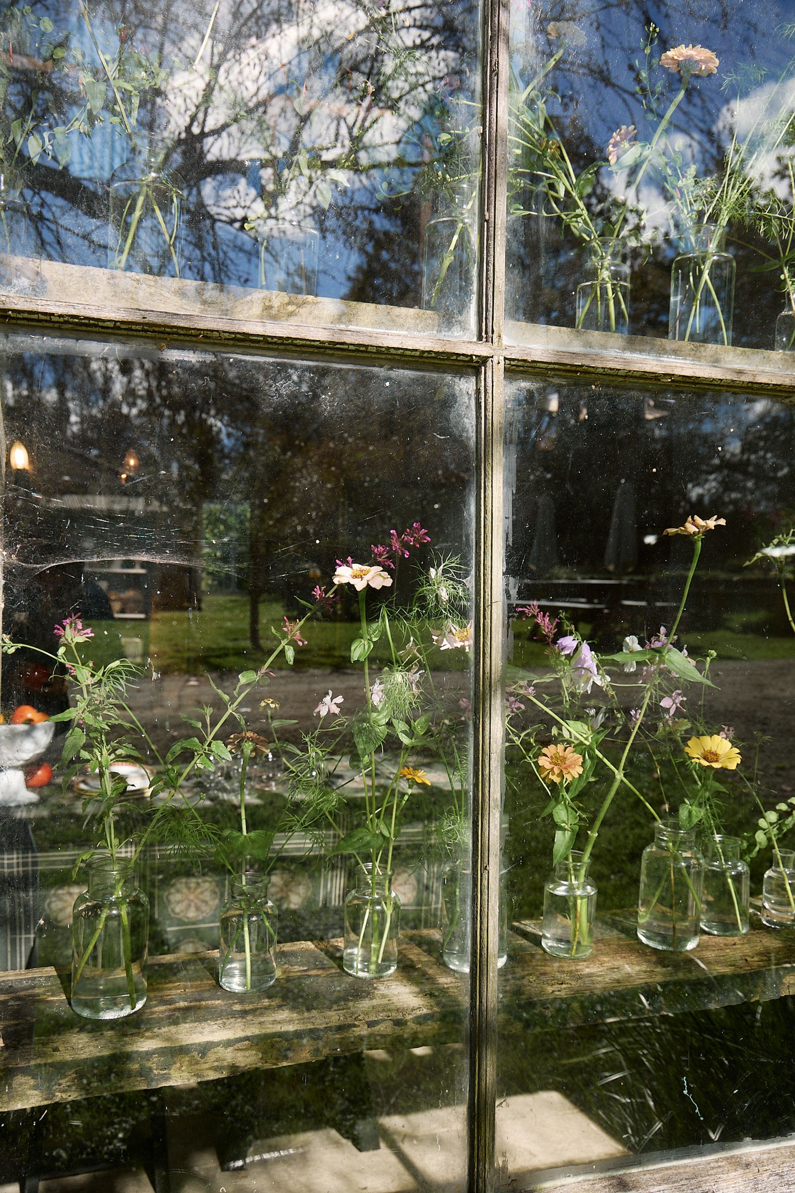 barn window pressed full of wild flowers in glass bottles in the sun