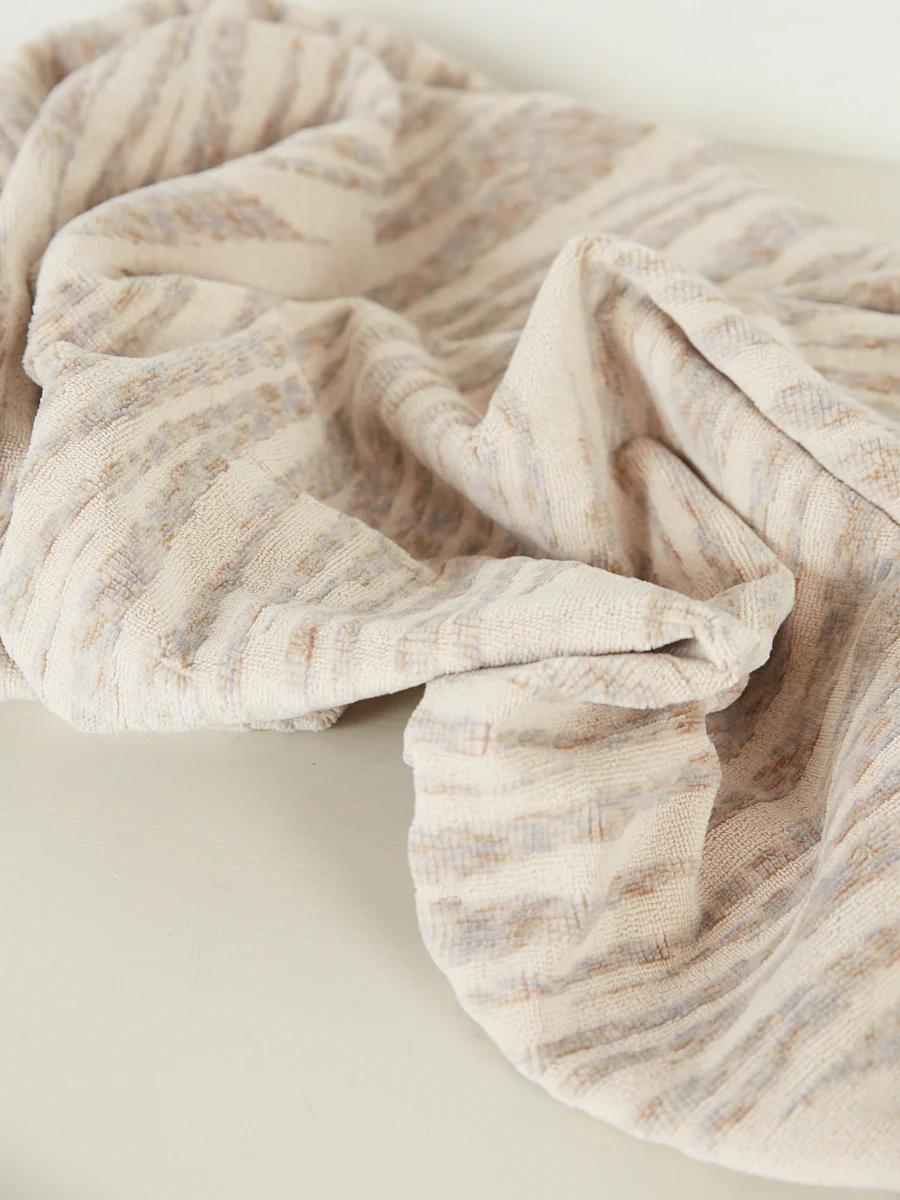 A beige towel with subtle stripes and pastel hues lies rumpled on a flat surface, creating soft folds and shadows.