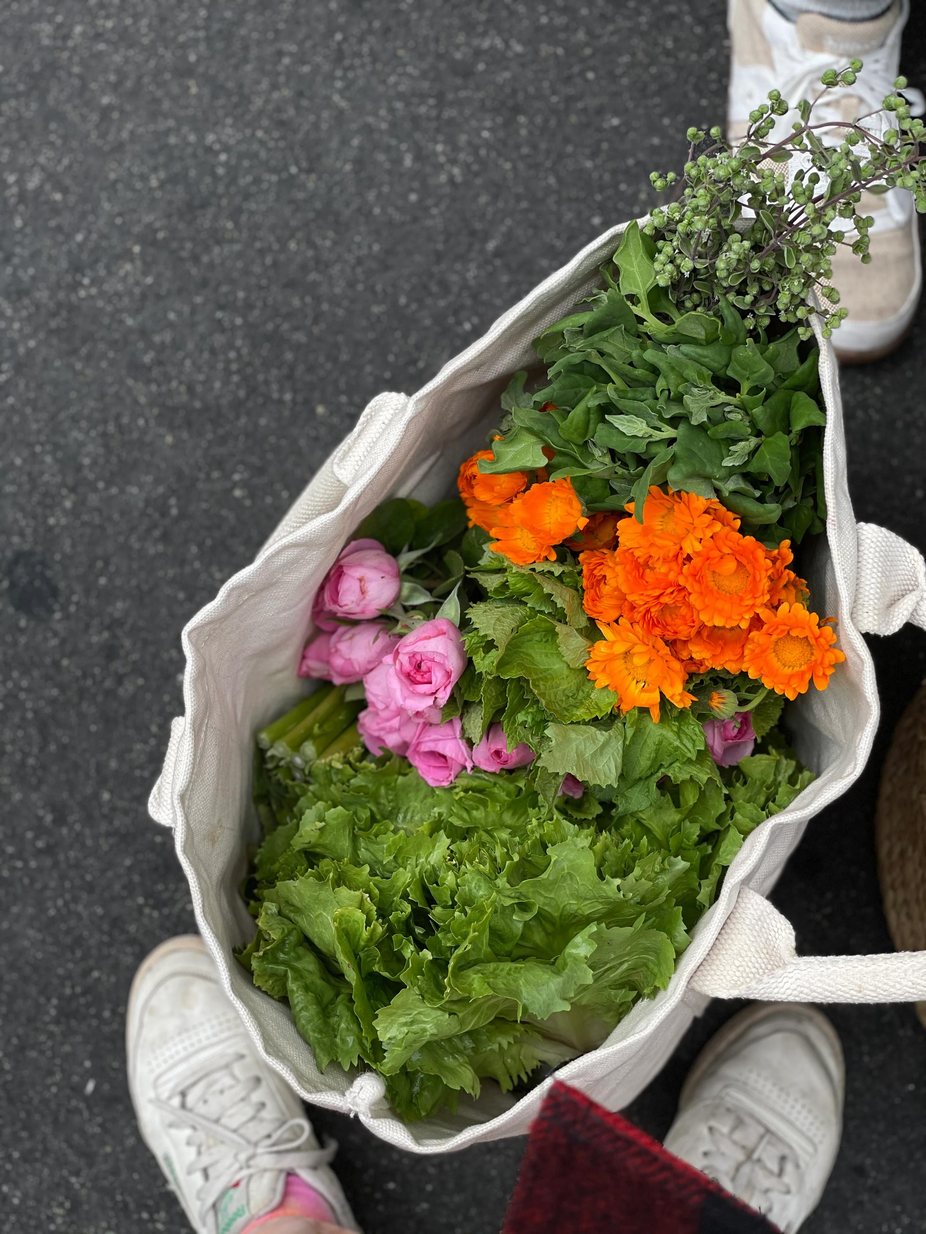 Canvas bag with fresh produce near person in white sneakers. Red shoes partially visible.