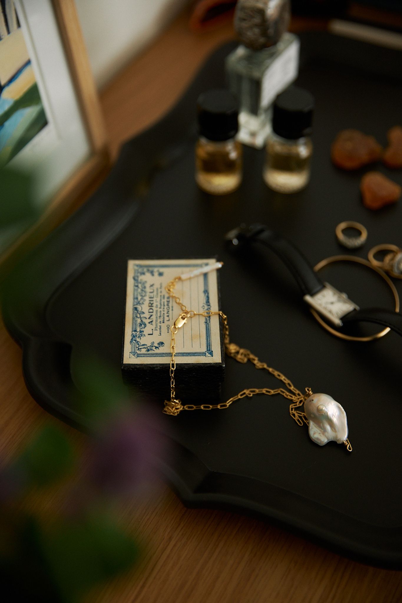 jewellery is strewn over a black tray with perfume bottle blurred in the background