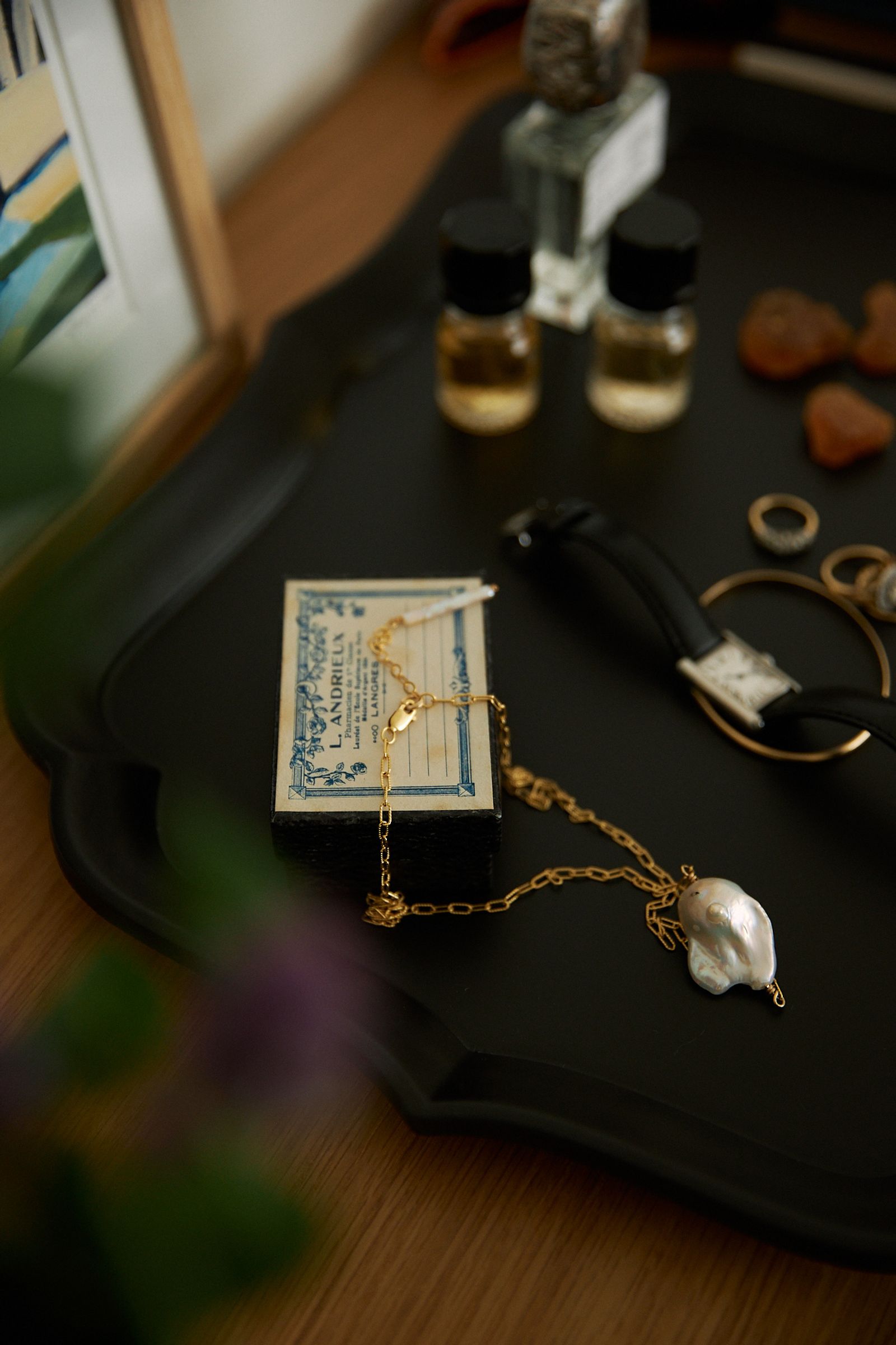 jewellery is strewn over a black tray with perfume bottle blurred in the background