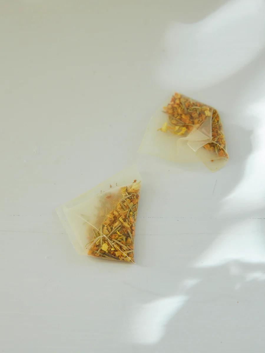 - Two pyramid tea bags with dried herbs on light surface. Soft shadows create serene atmosphere. Premium small batch teas.