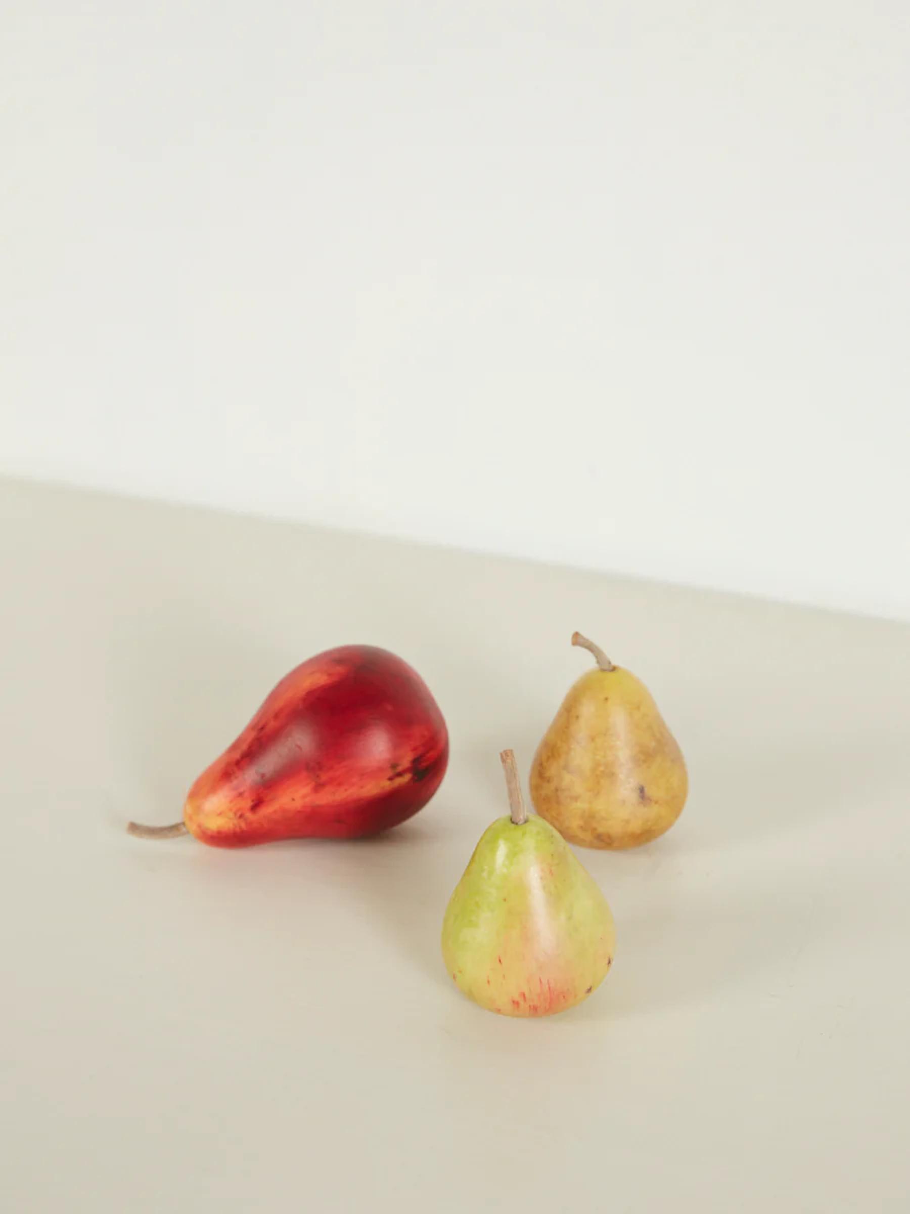 Three pears on light surface: one red, two yellow-green. Plain background reminiscent of Carrara marble showcases fruit.