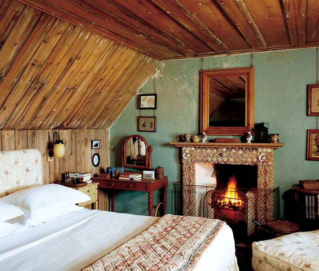 Rustic bedroom with wooden walls. Queen bed, lit fireplace, and vintage vanity. Mirror above mantel. Jura-inspired decor.