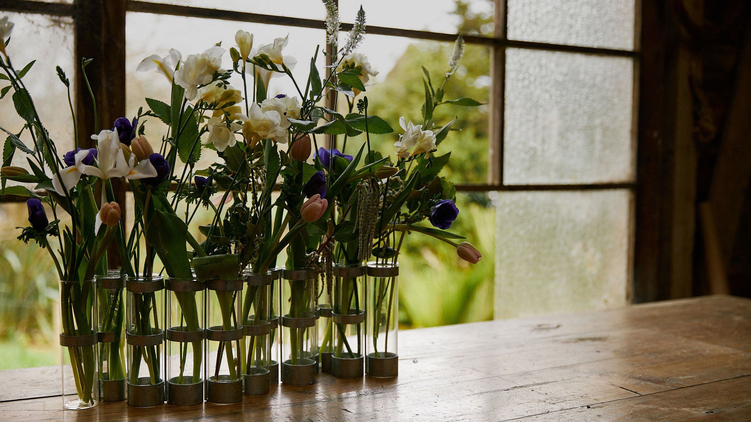 Wooden table with glass vase filled with spring blooms beside a window
