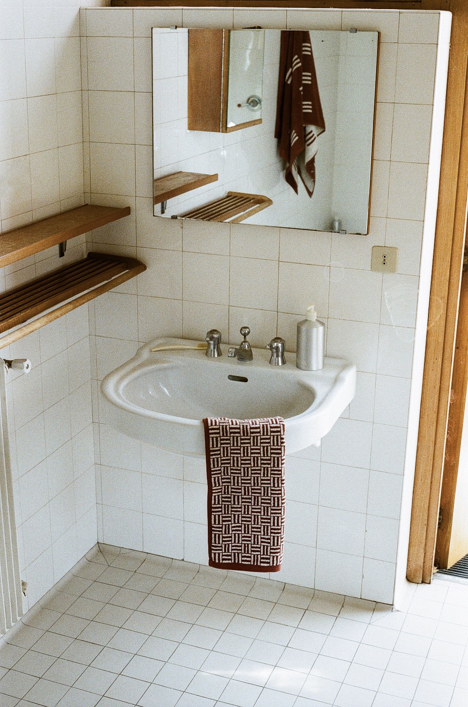 a white tiled bathroom with wooden accents is softened by mud brick and creme coloured organic towelling