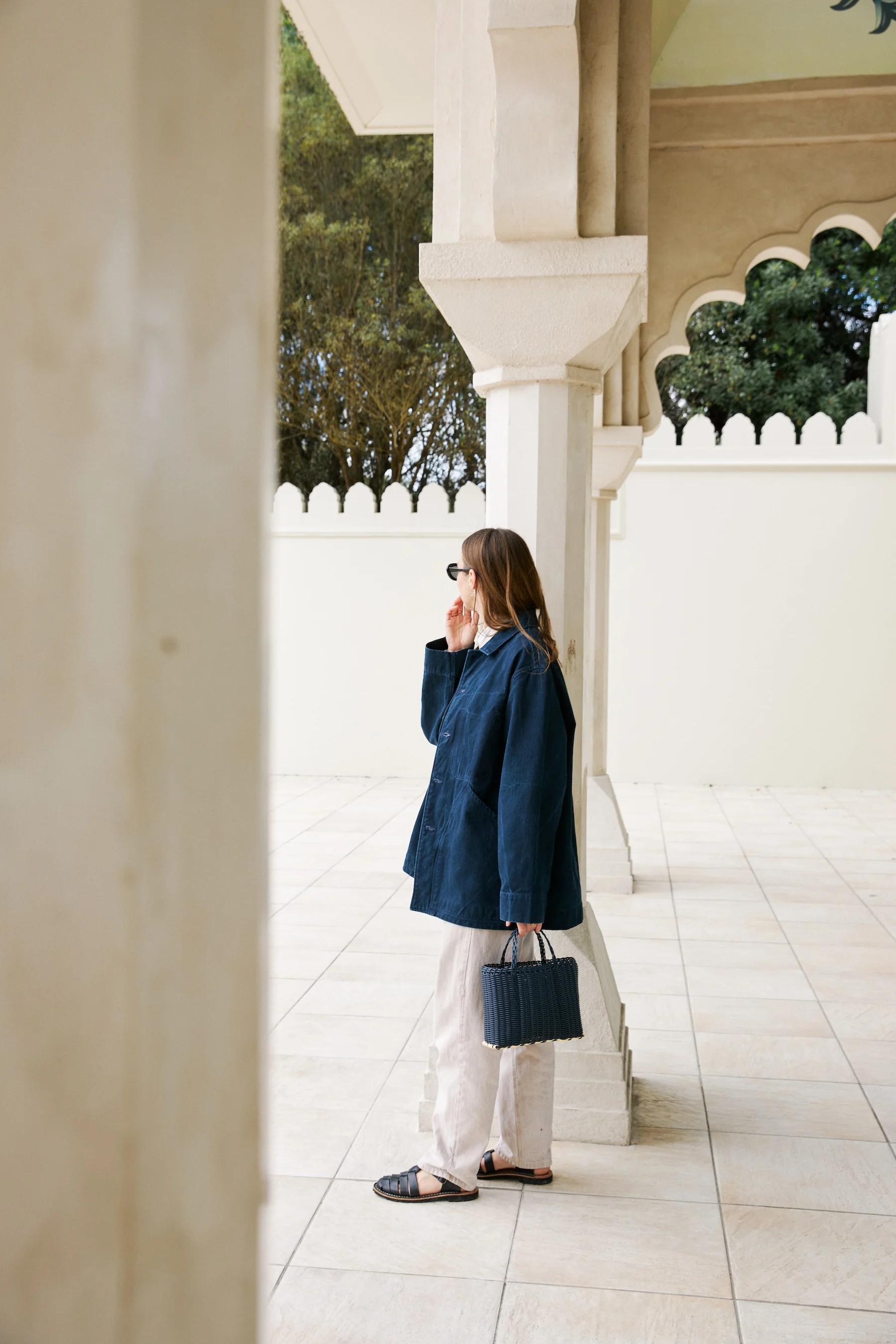 Dark blue jacket from the side worn open over pale trousers. 