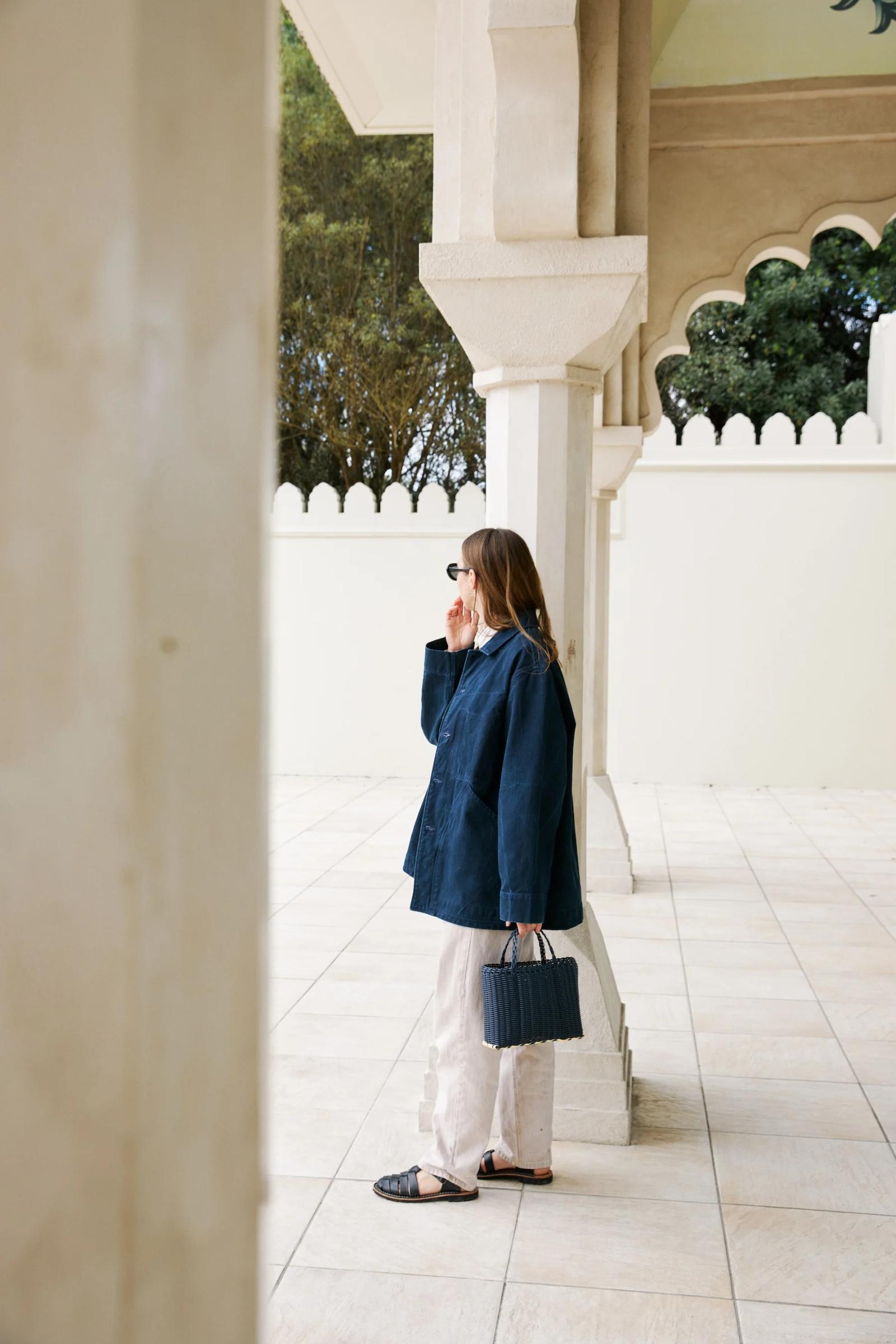 Dark blue jacket from the side worn open over pale trousers.