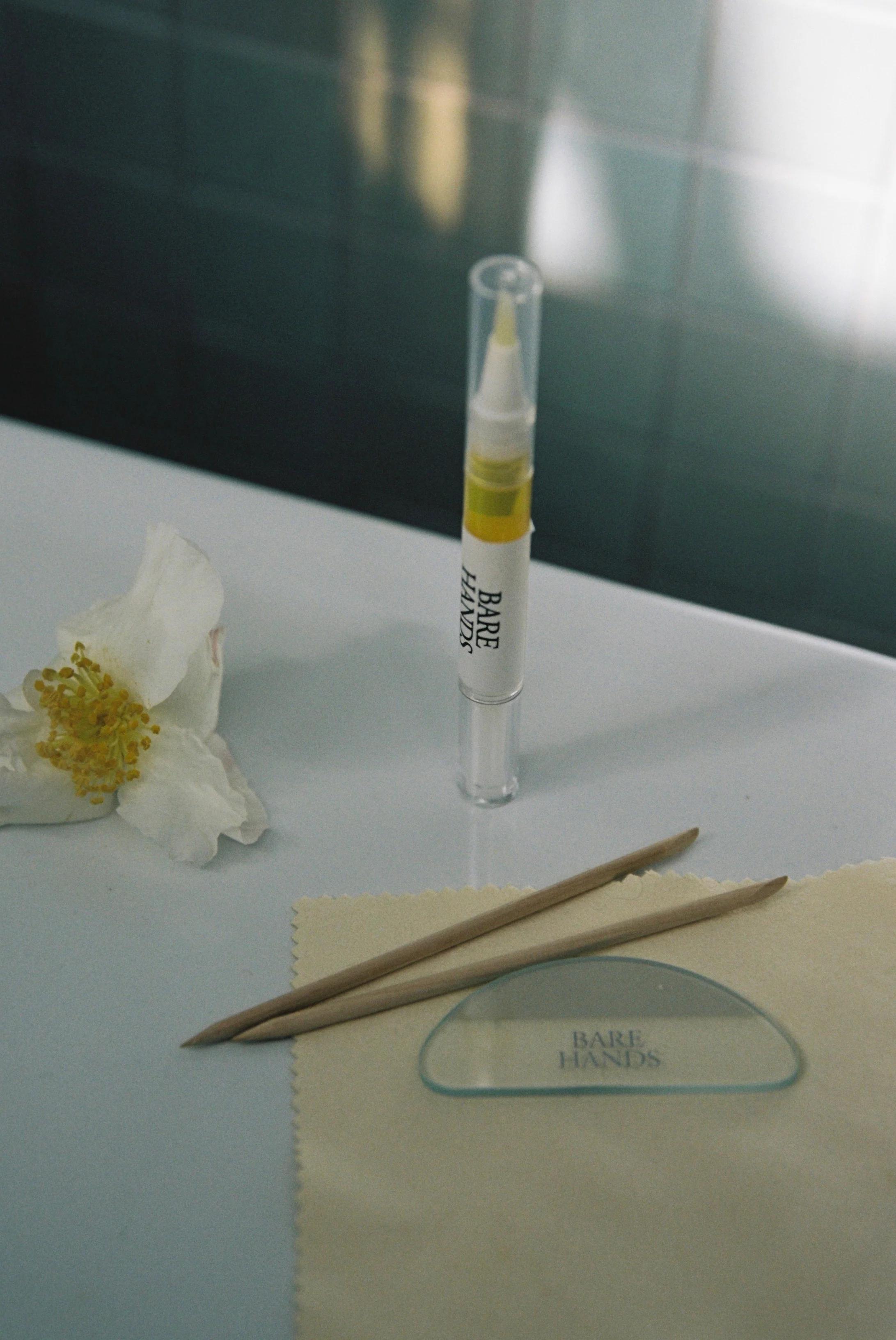 Manicure tools including "Bare Hands" products, wooden pushers, and a glass file. A white flower adds a touch of nature to this self-care scene.