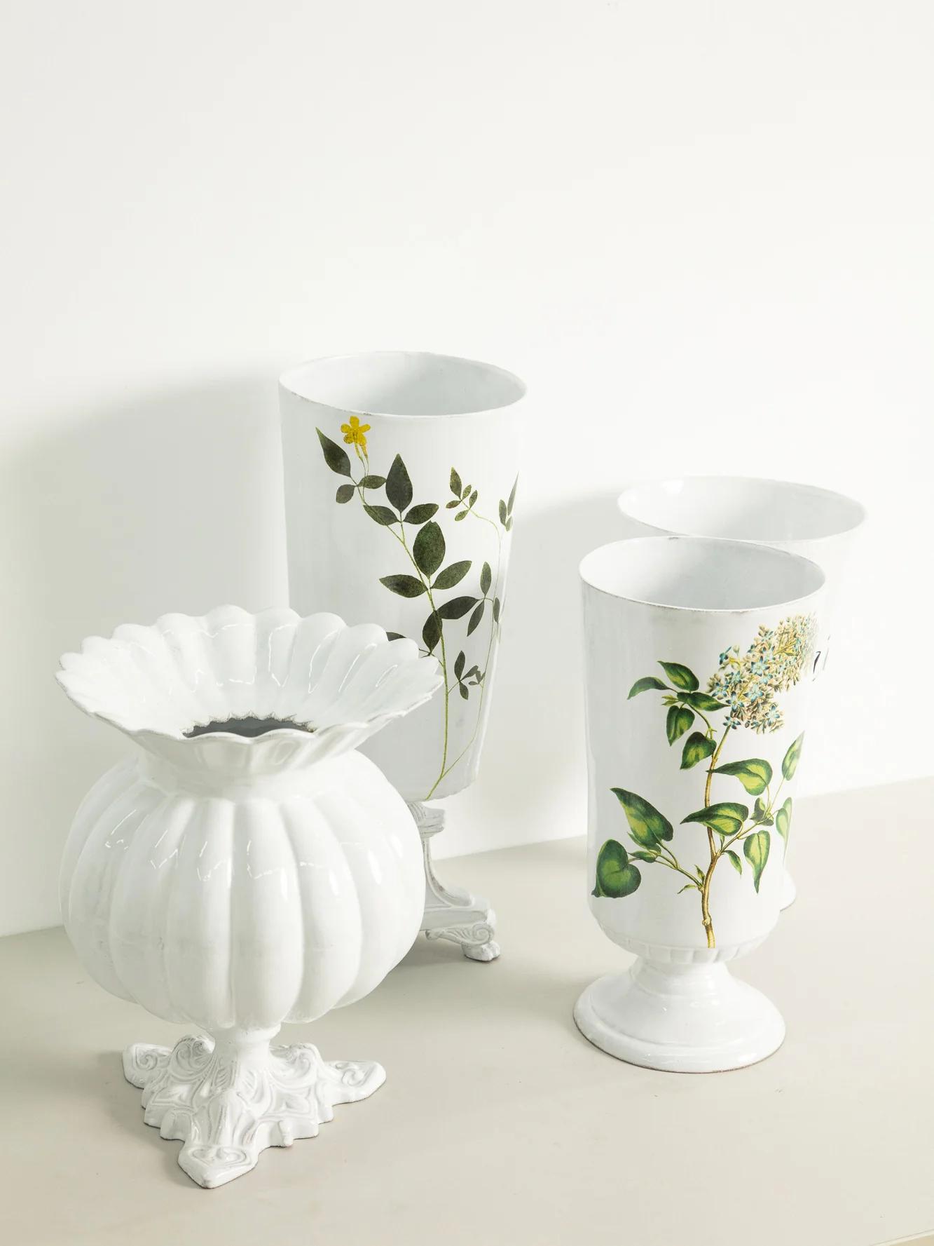 Three white ceramic vases with botanical illustrations. Round vase with scalloped rim, two taller cylindrical vases with plant designs.