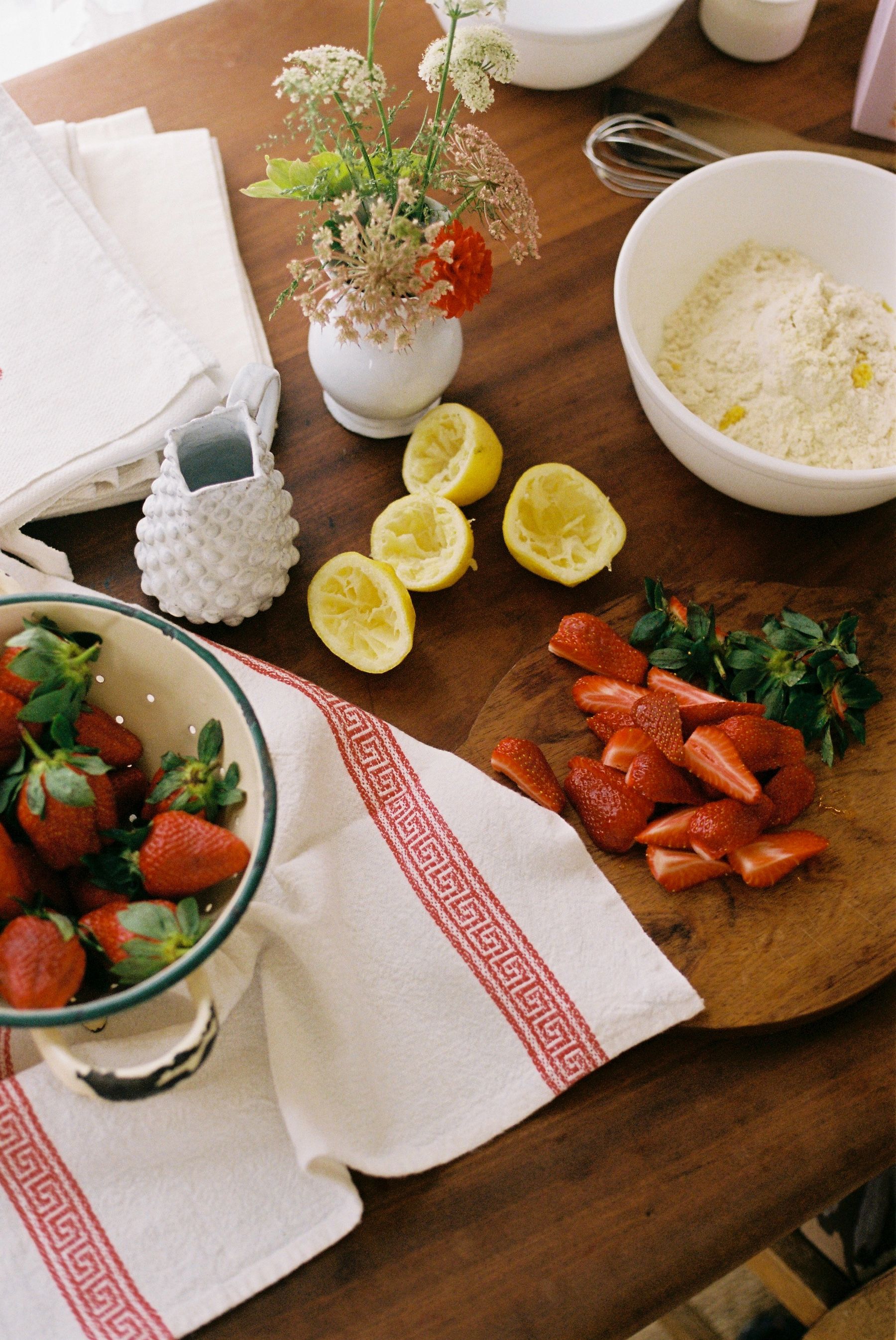 kitchen bench with freshly cut strawberries, squeezed lemons and flowers