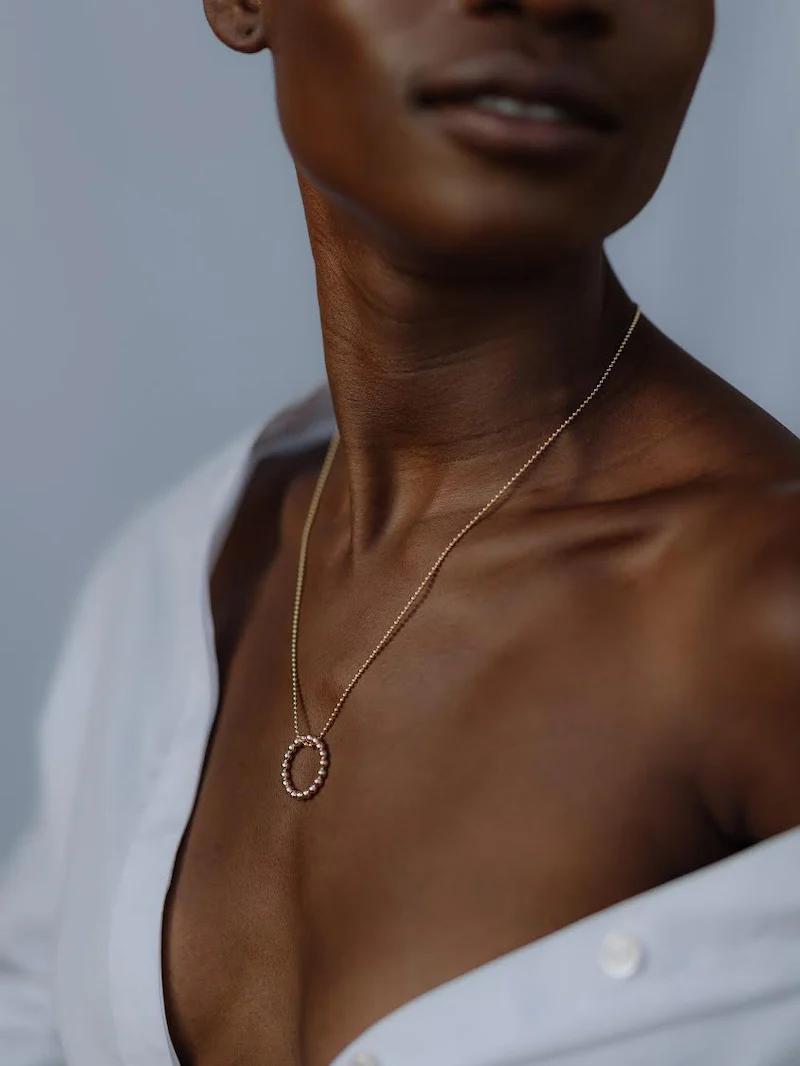 Close-up of person in open white shirt wearing gold necklace with circular pendant.