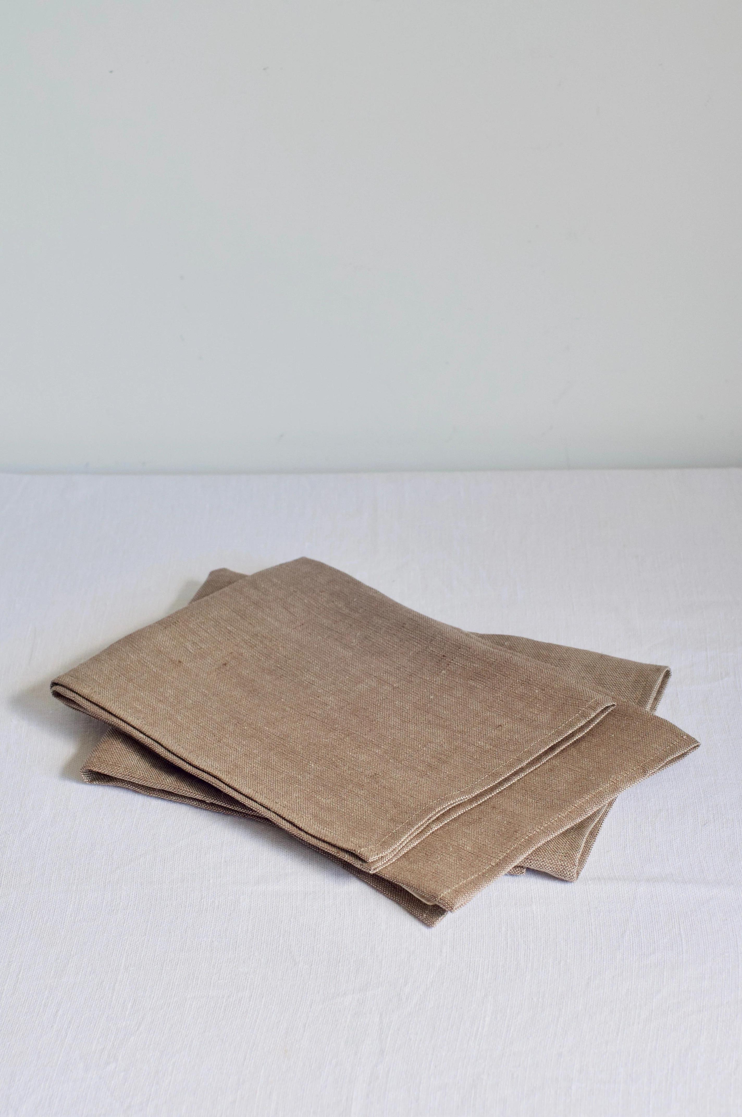 Three folded beige napkins on white surface. Layered, neat appearance. Simple, elegant Italian brand aesthetic.