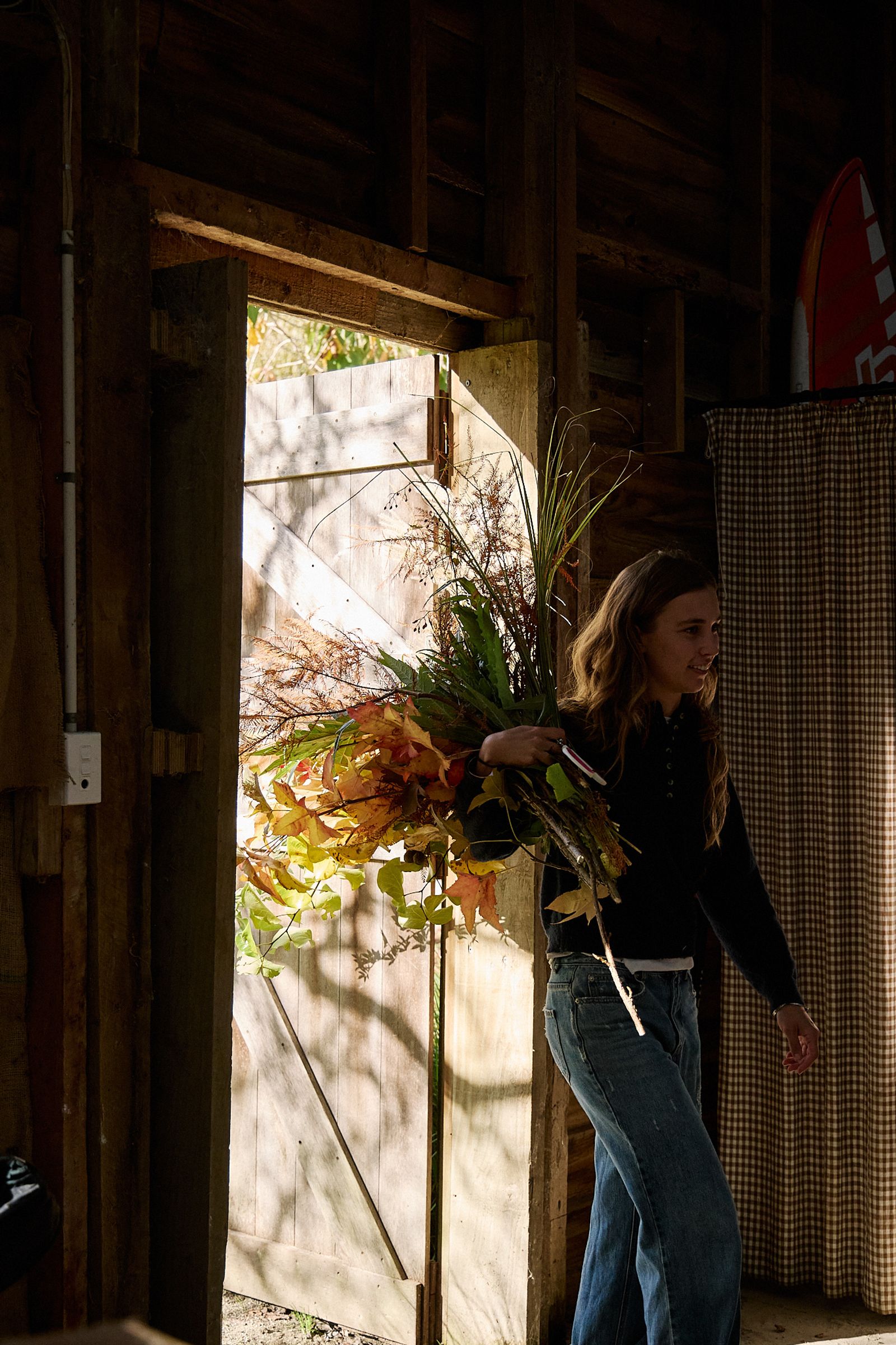 Aila walking through barn doors holding a huge armful of blooms
