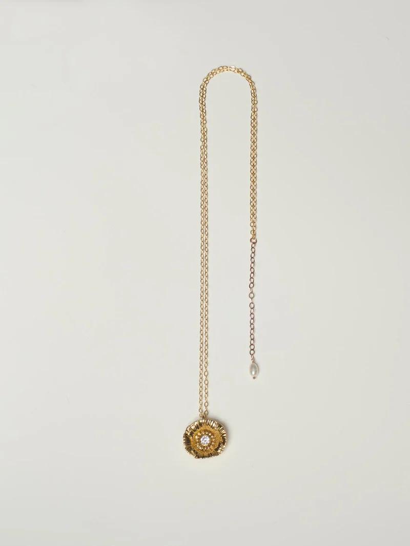 Gold necklace with circular pendant, intricate detailing, central gem. Chain with smaller loop and pearl.