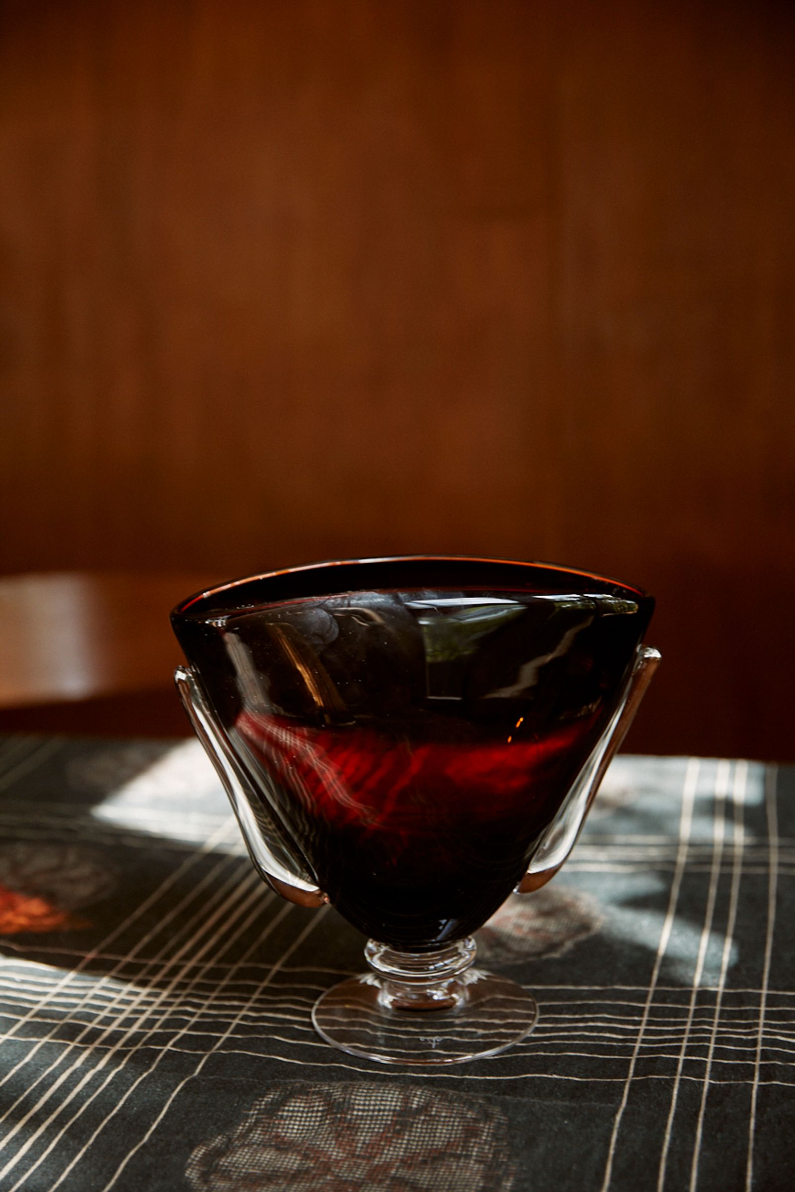 dark red glass vase sits on a floral patterned tablecloth in midcentury home