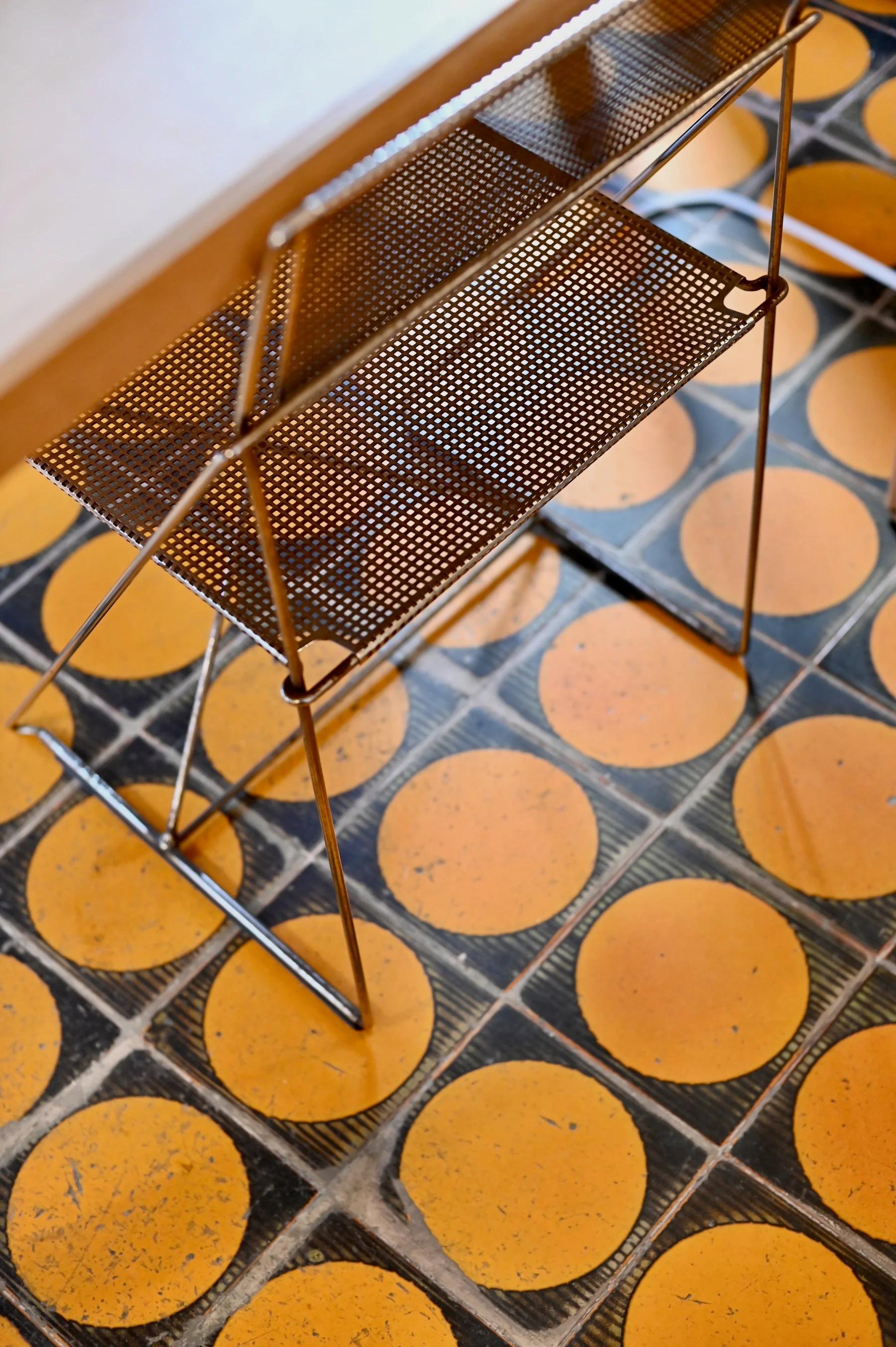 Lightweight metal stand with perforated shelves on retro-style patterned floor. Top-down view.