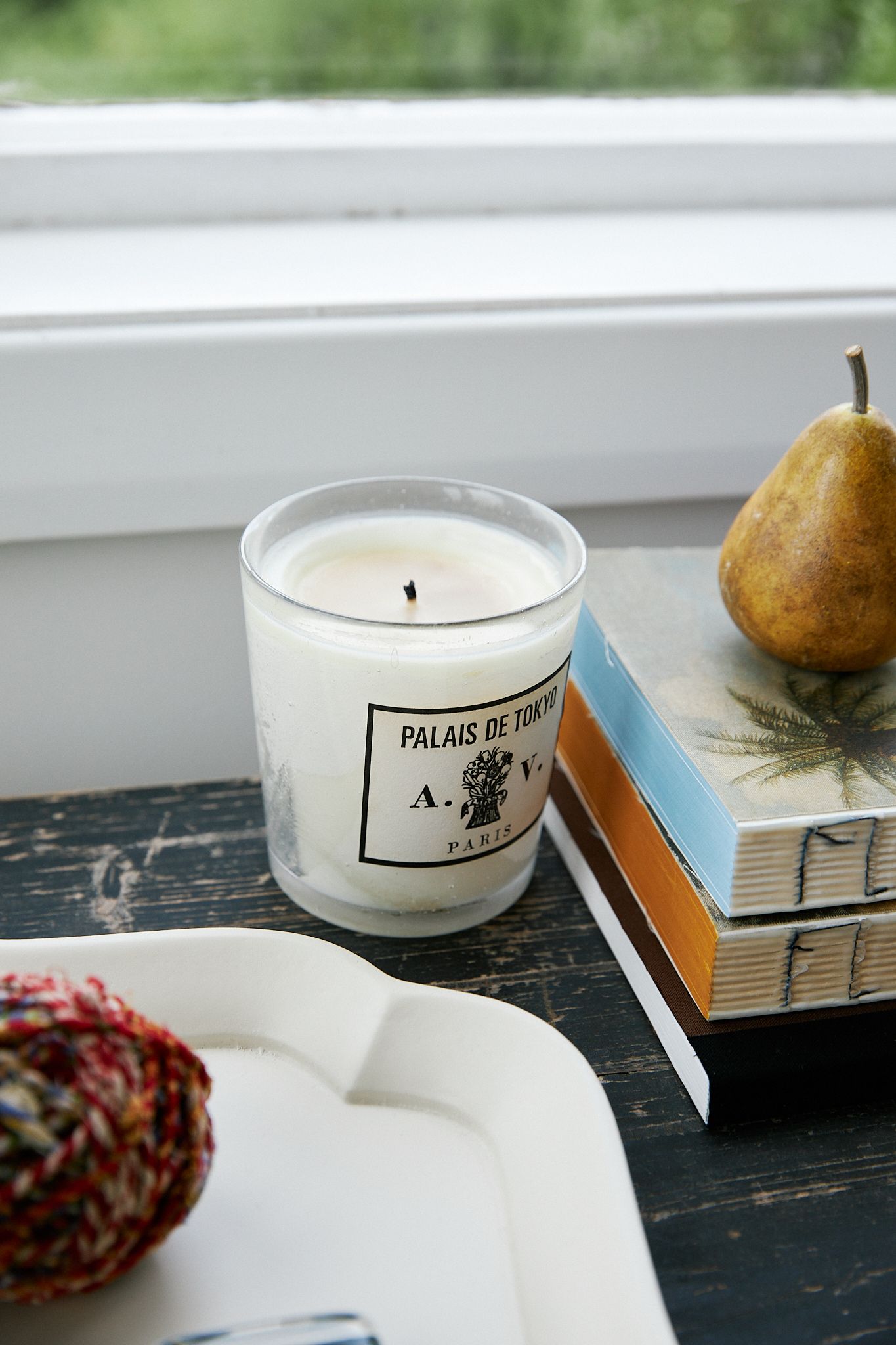 A white candle sits amongst a desk set up near the windowsill