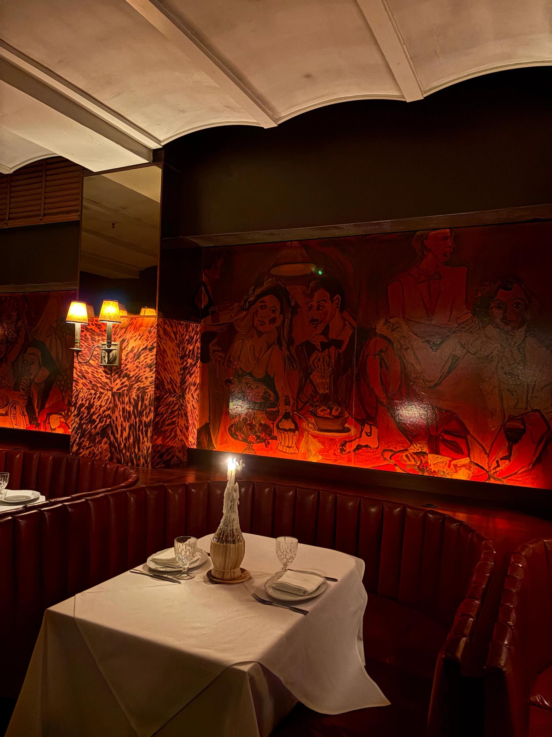 candlelit dinning booth with hand painted murals on the wall in red tones