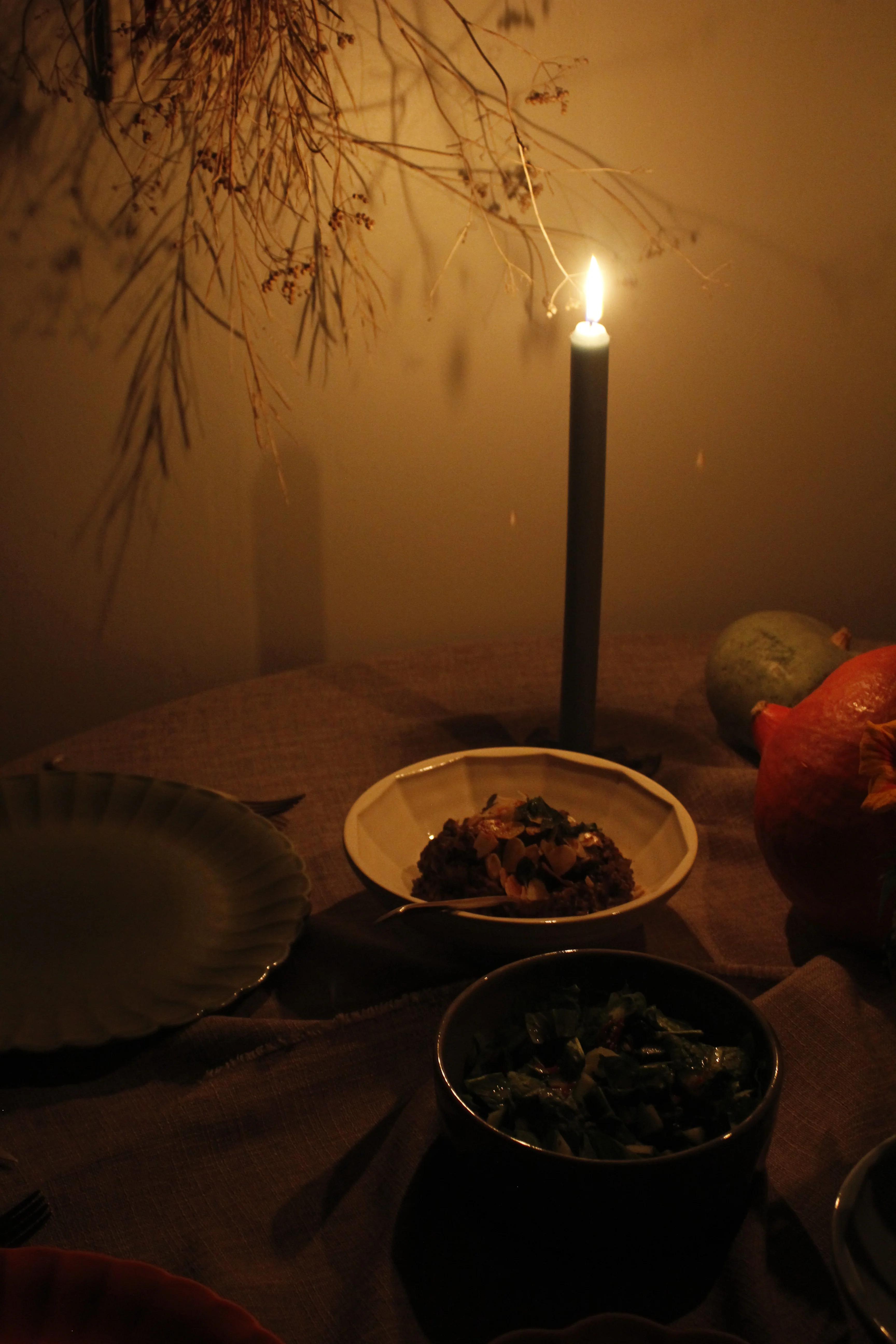 A dimly lit dining table with a candle, a plate of Palestinian recipes, greens, and gourds creates a warm, cosy atmosphere.