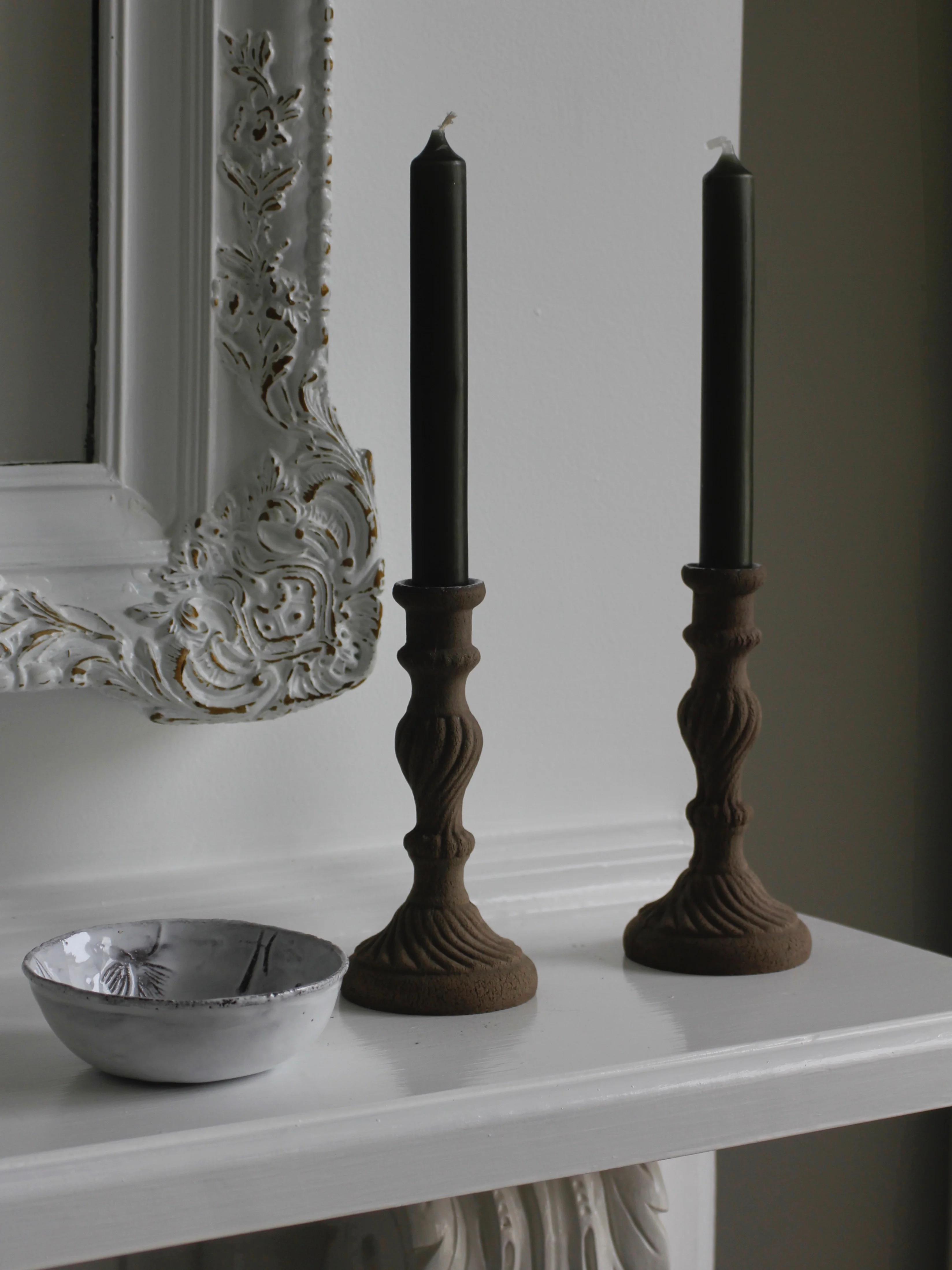 White mantel with green candles in brass holders. Grey ceramic bowl with black details. Astier de Villatte mirror in background. Cosy winter setting.